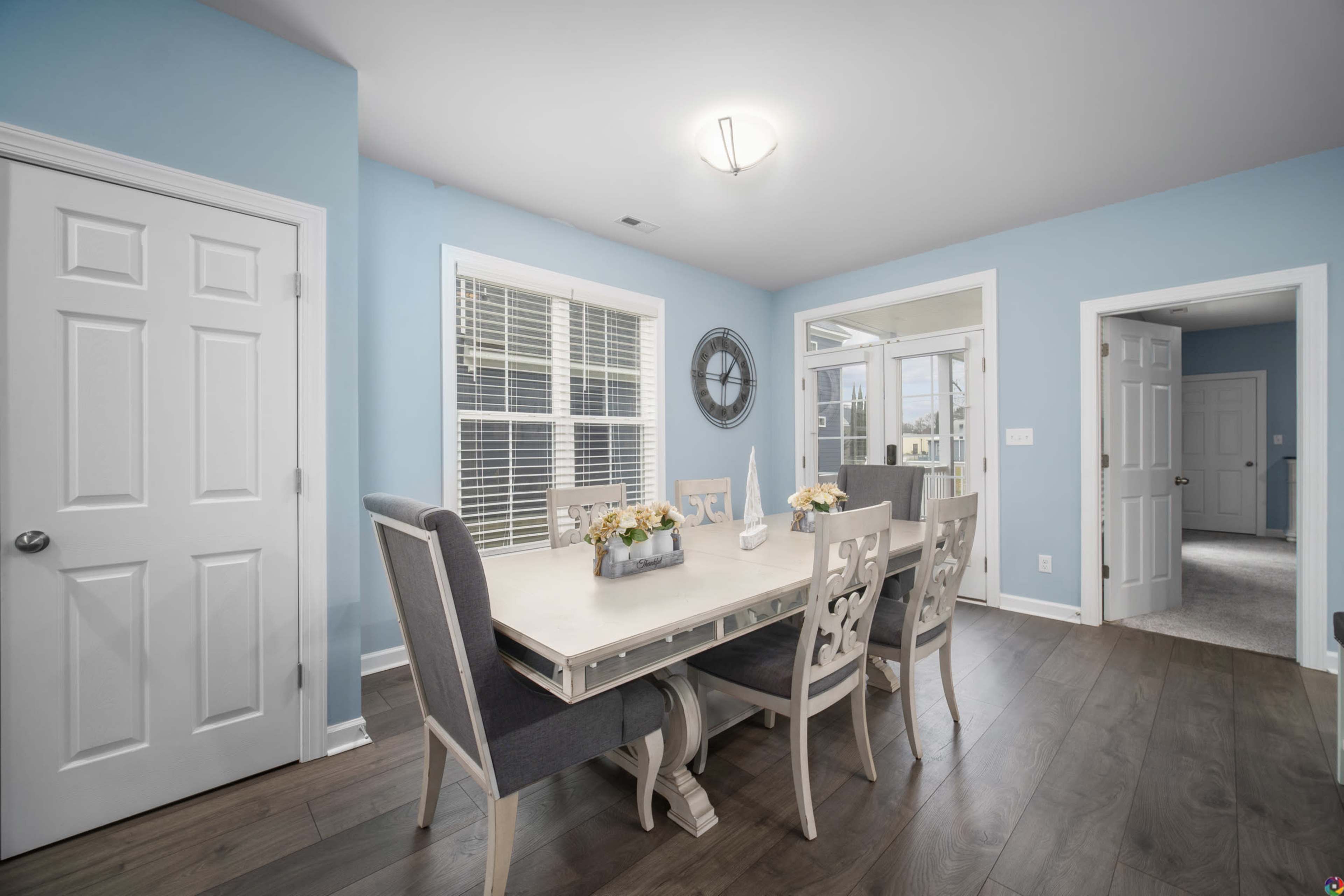 A dining area with a light blue wall, a large table surrounded by upholstered chairs, and doors leading to an outdoor space.