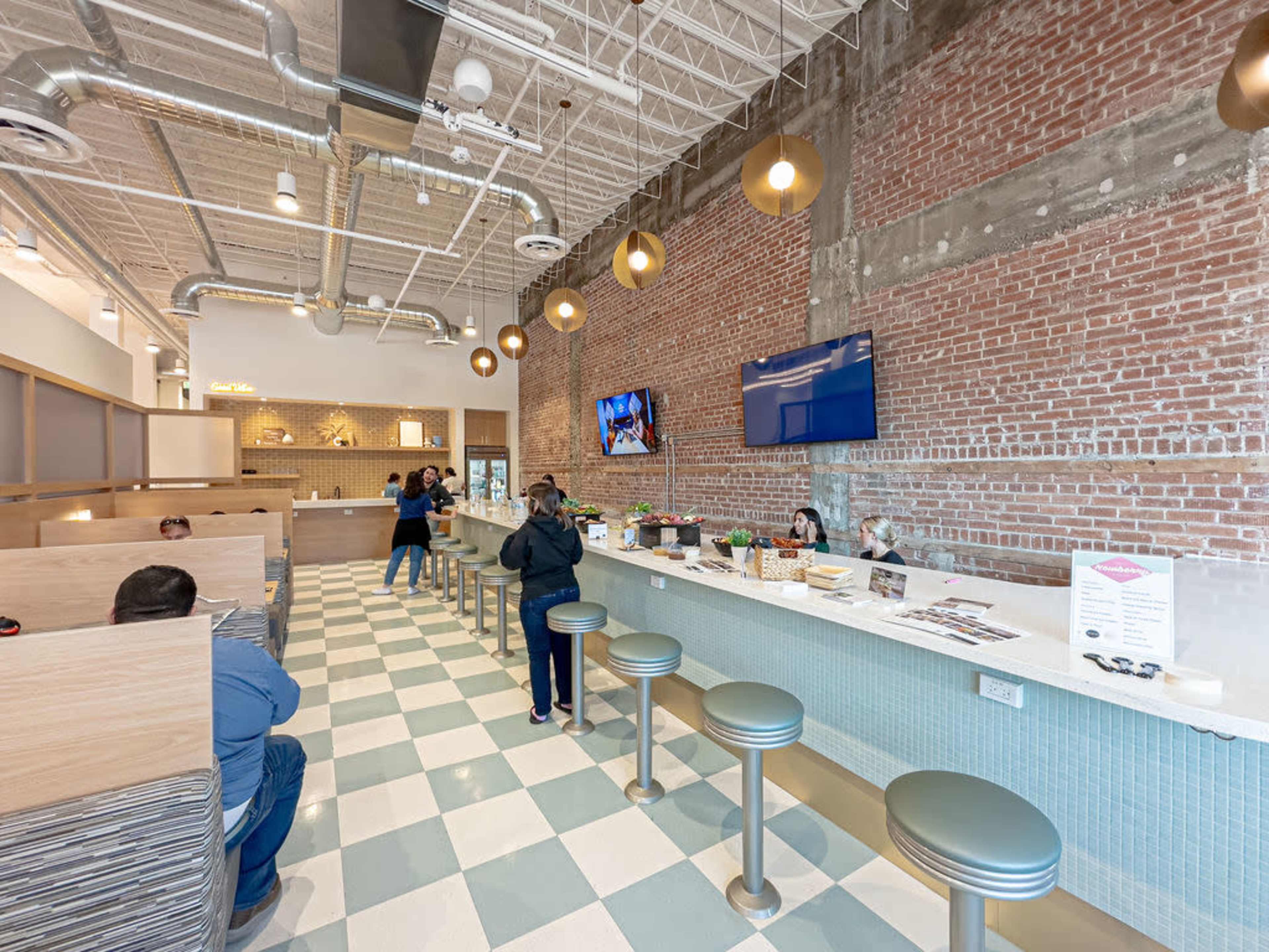 The image shows a modern café interior with a mix of seating options, exposed brick walls, and pendant lighting.