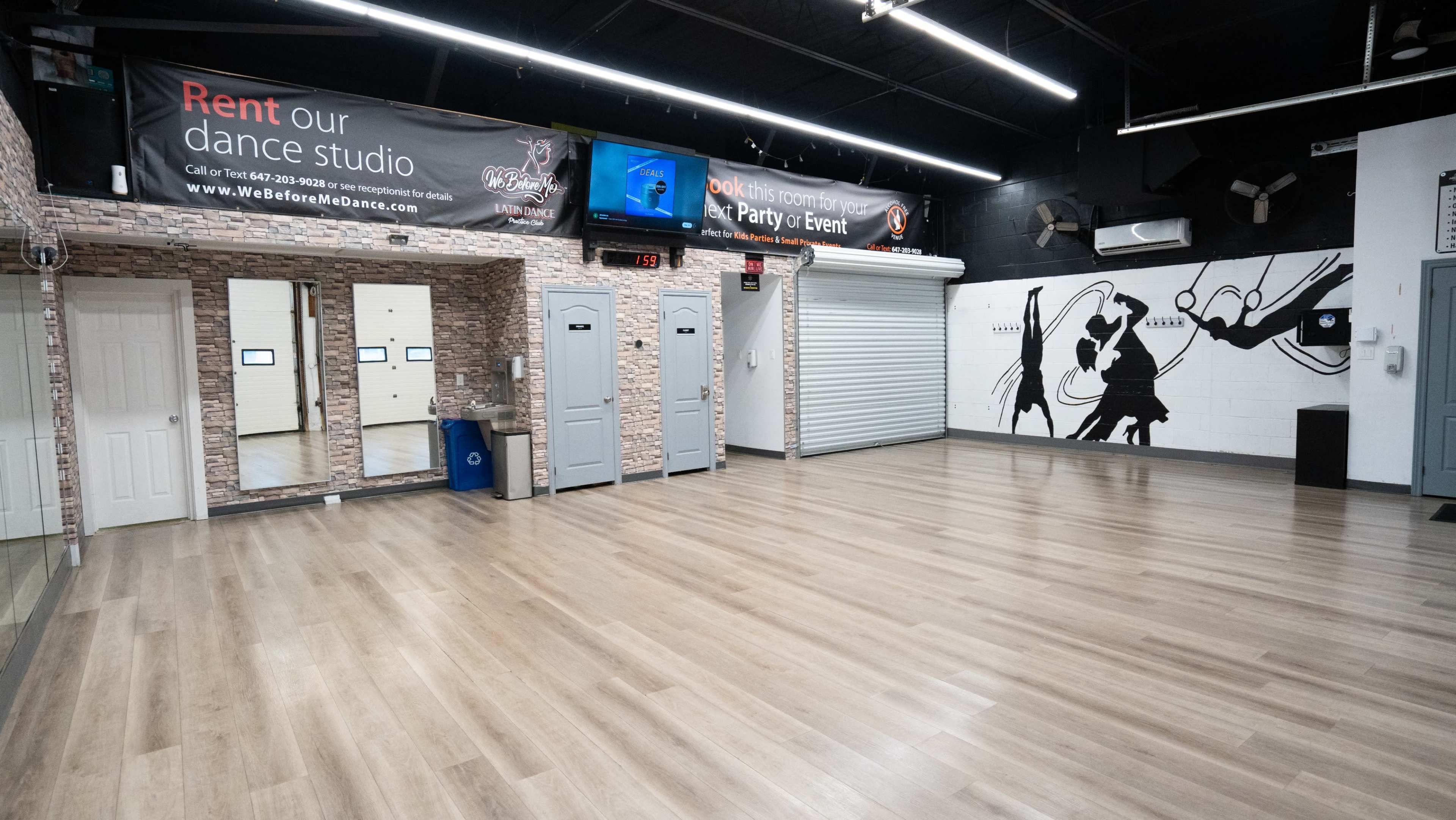 The image shows a dance studio with a wooden floor, mirrors on one wall, and a mural depicting dancers on another wall.