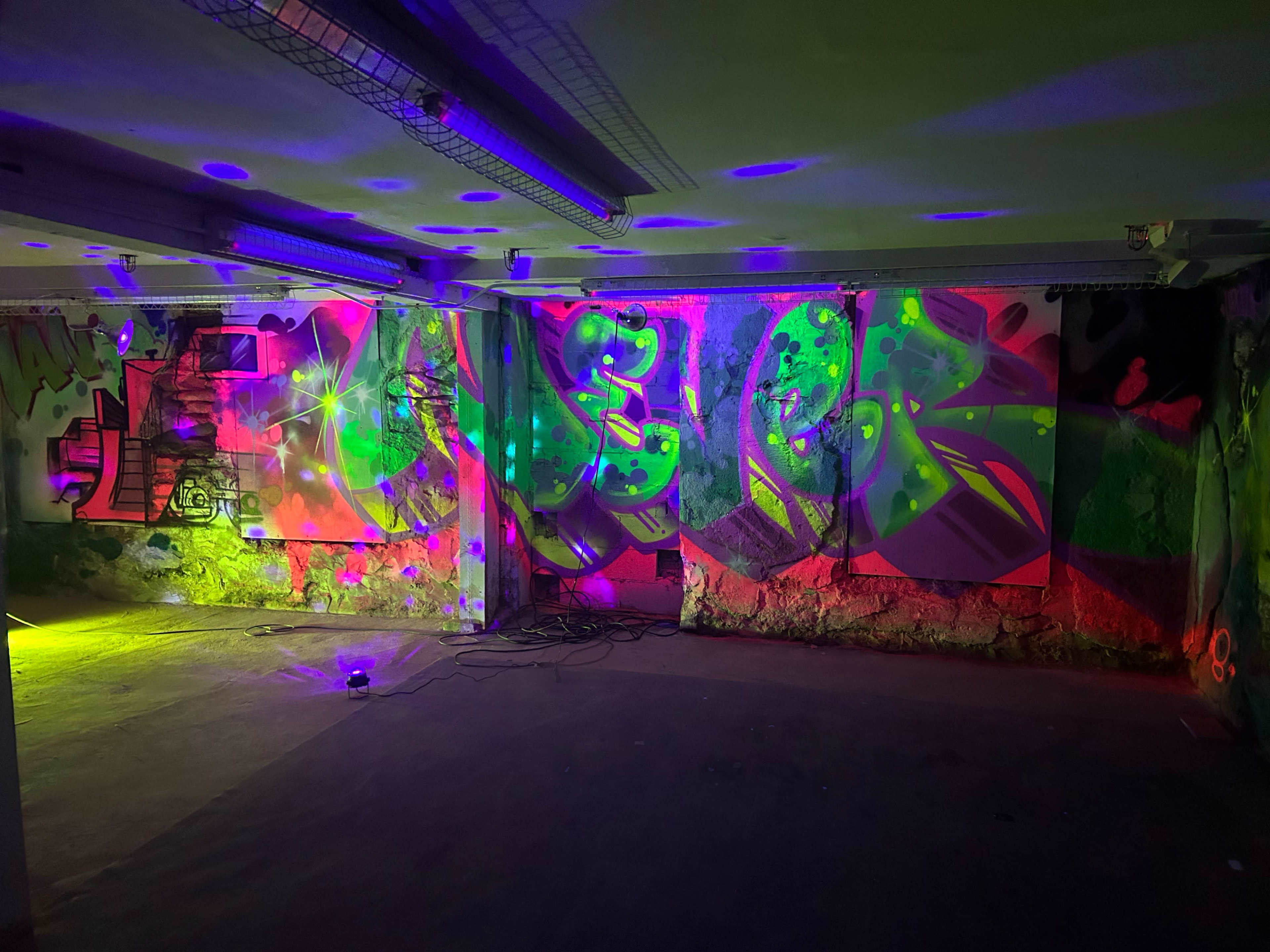 A dimly lit room with colorful graffiti on the walls and vibrant lighting effects creating a party atmosphere.