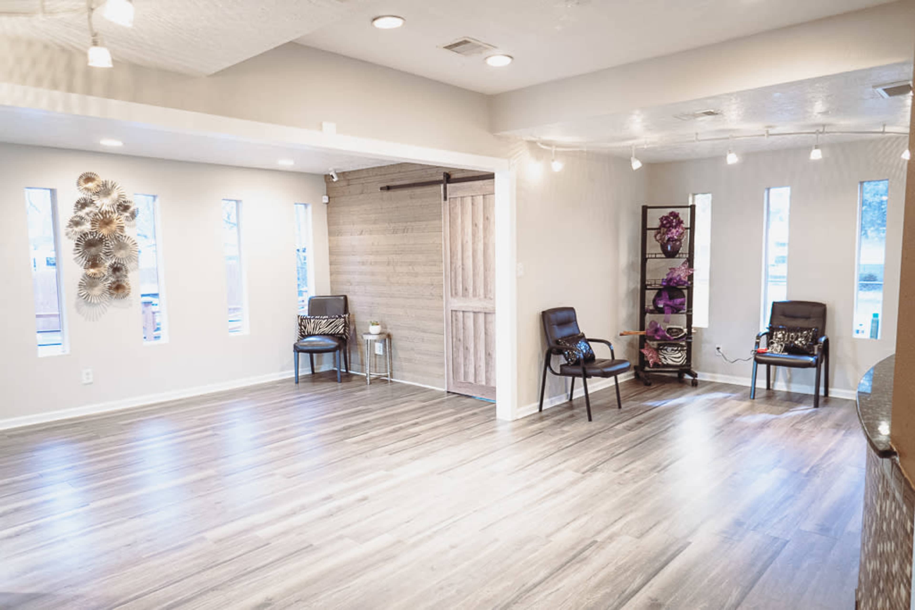 A spacious room with light wooden flooring, featuring two chairs, decorative wall elements, and a sliding barn door.