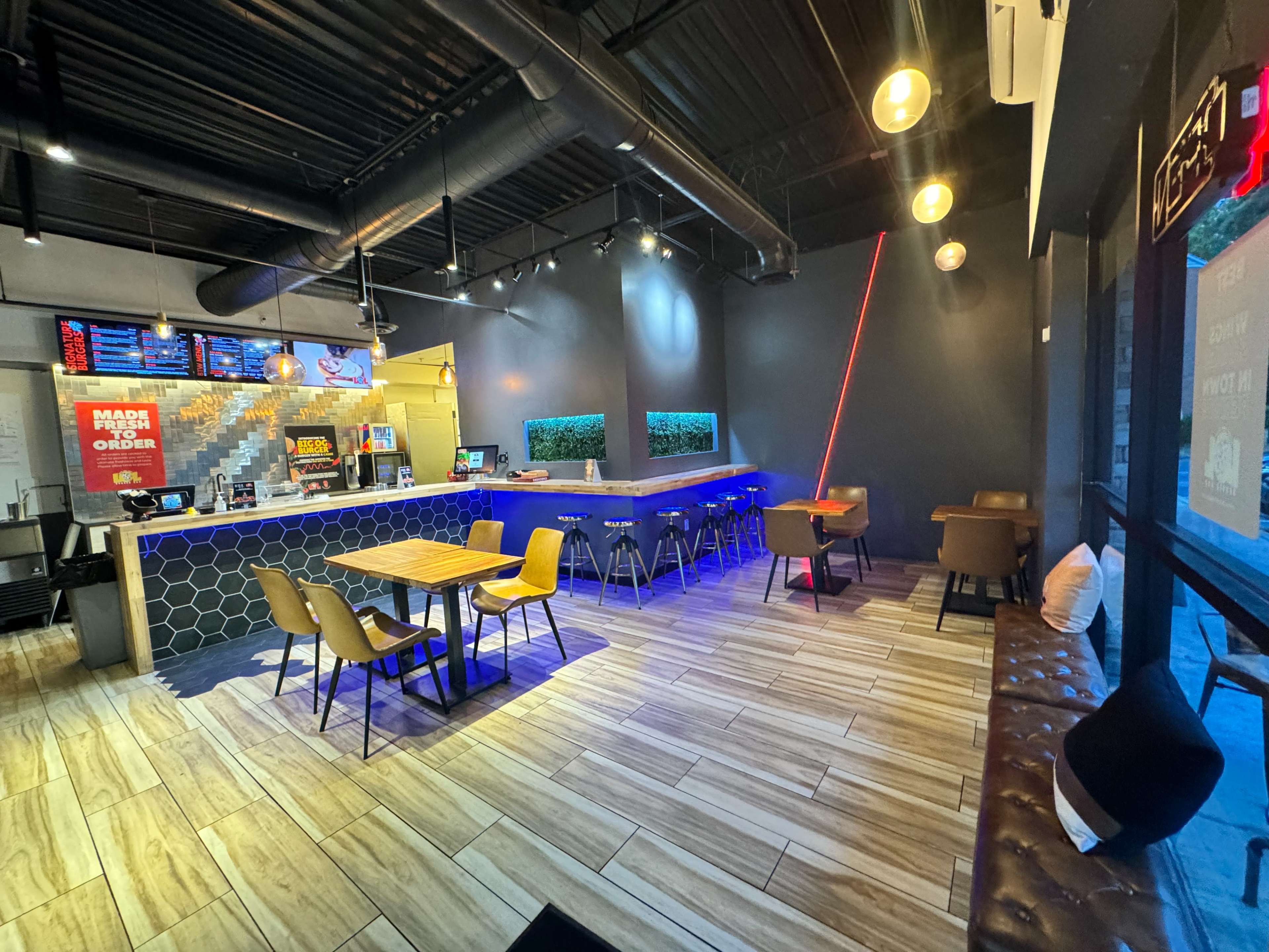 A modern restaurant interior with a counter, seating areas featuring wooden tables and chairs, and decorative lighting.