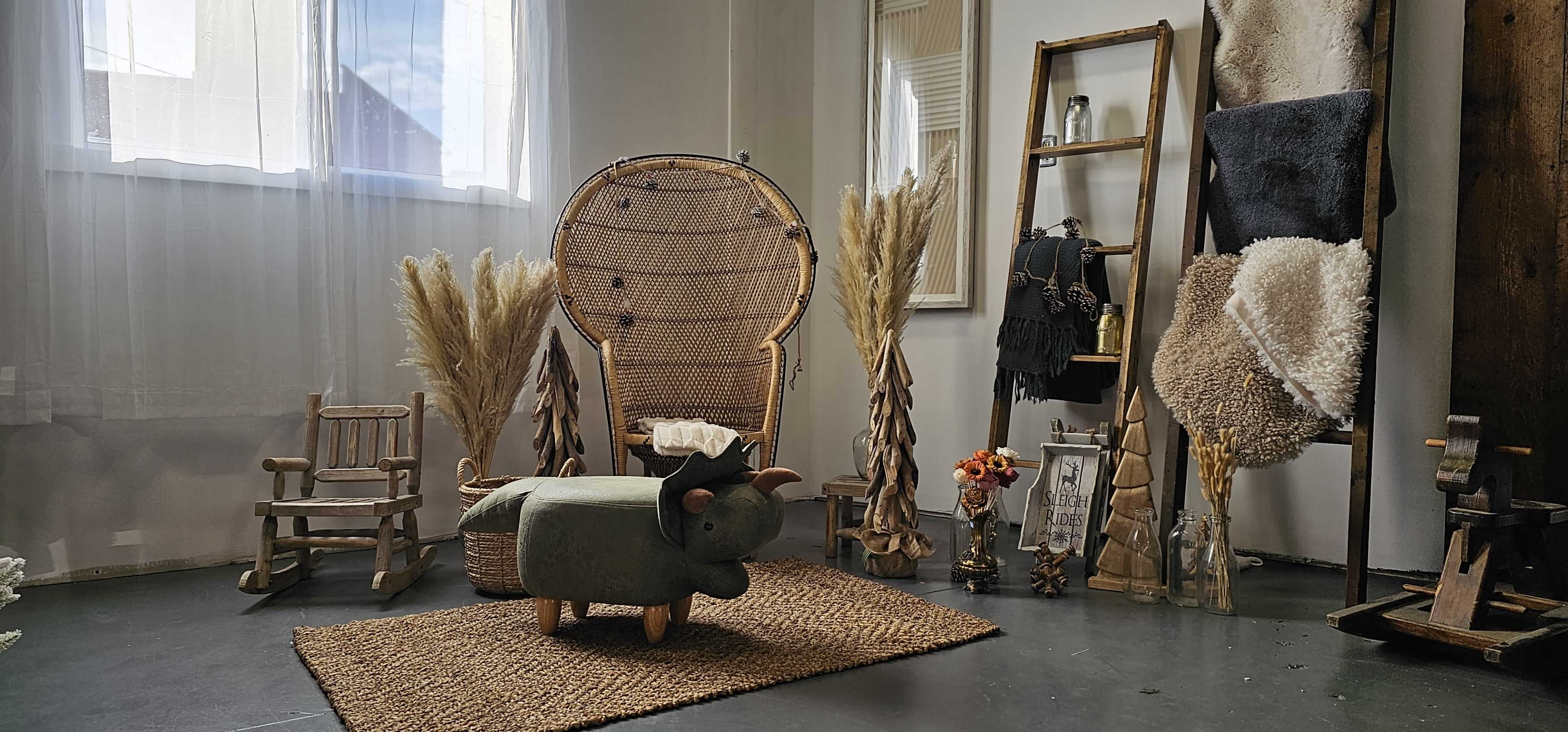 The image features a cozy interior scene with a woven chair, a decorative stool shaped like a bull, and various plants arranged around a textured rug.