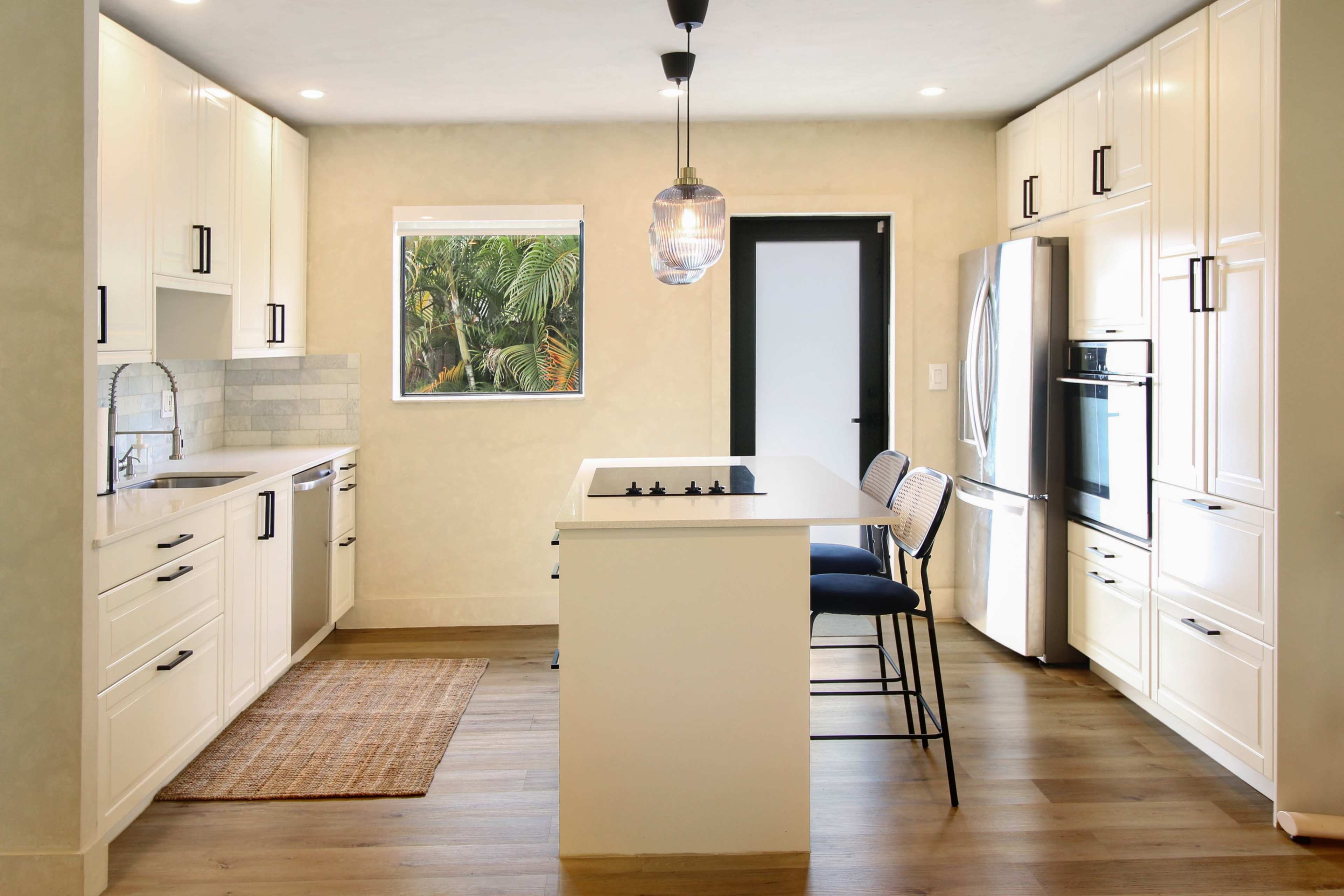 A modern kitchen features white cabinetry, a central island with bar stools, and stainless steel appliances.