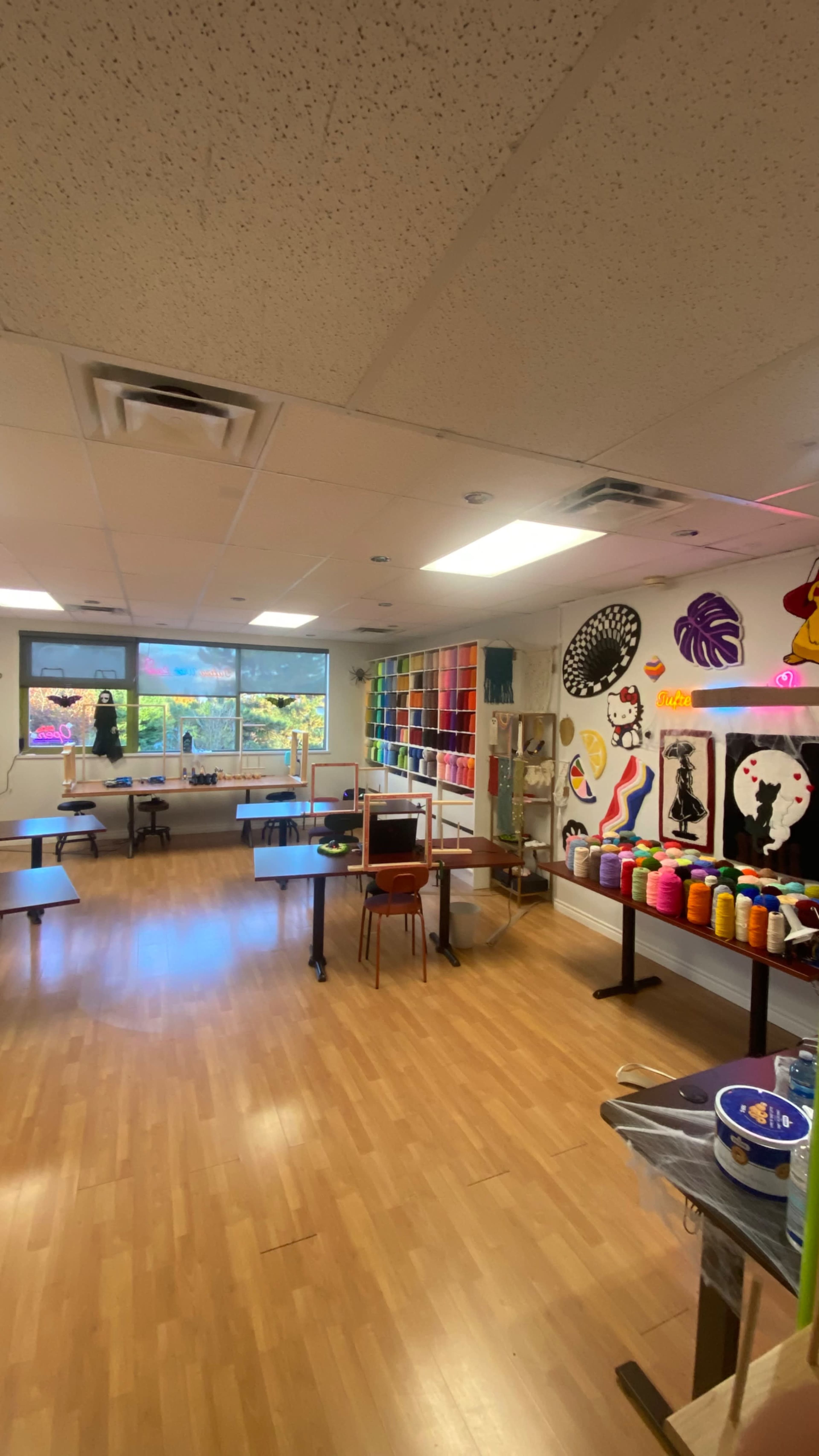 The image shows an art classroom with tables, chairs, and colorful supplies organized on shelves against the walls.