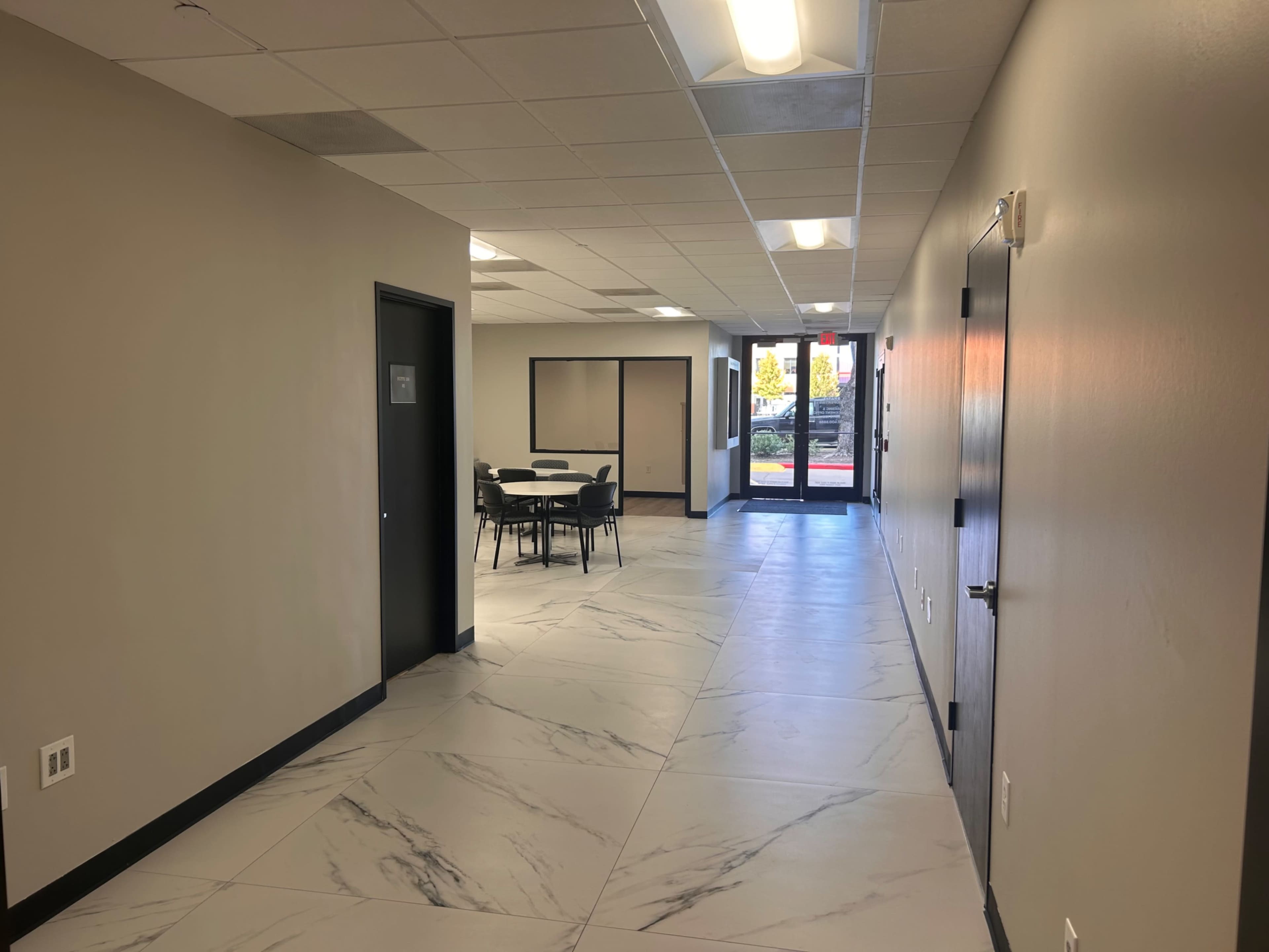 A hallway with a tiled floor leads to a glass door at the end, with a seating area visible on one side.