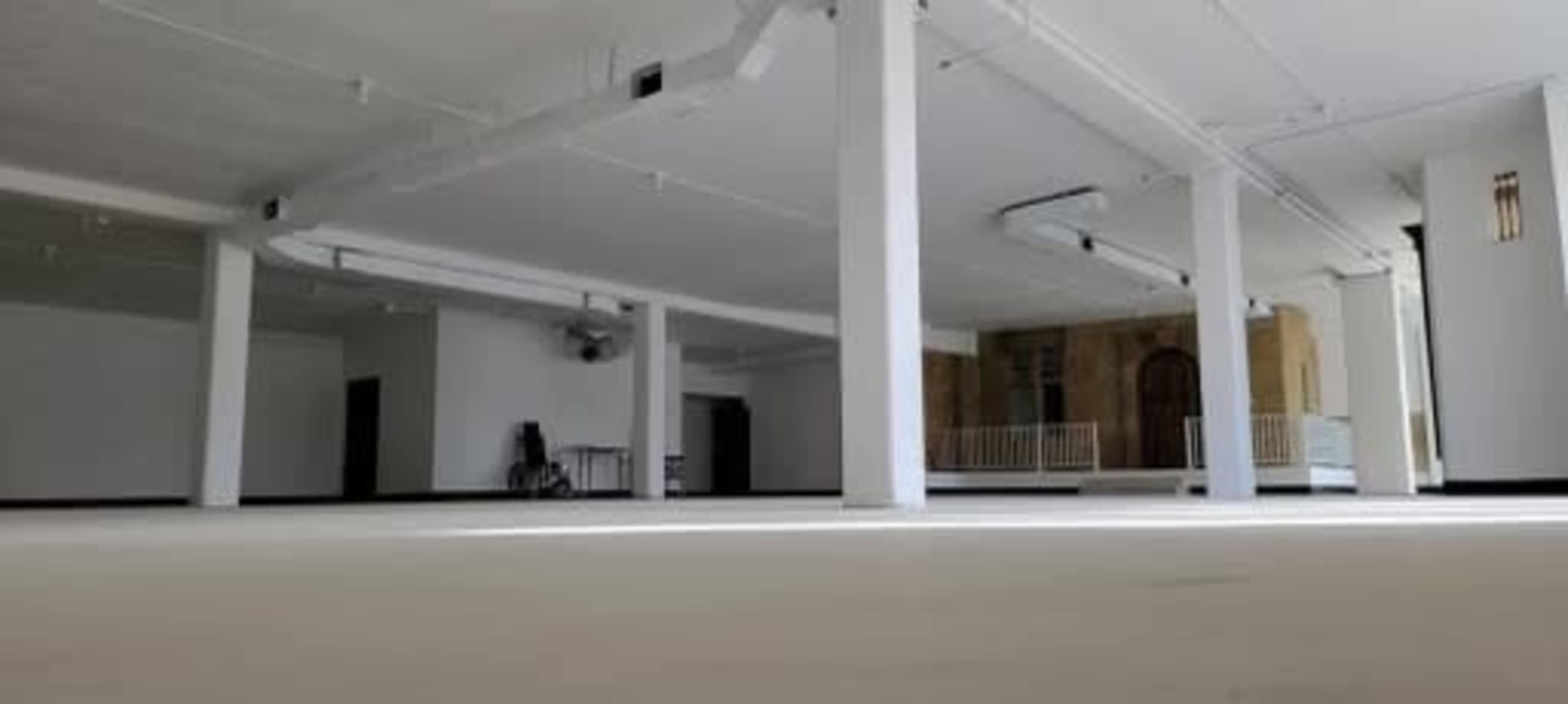A spacious, empty indoor area with white walls, concrete flooring, and several columns supporting the ceiling.