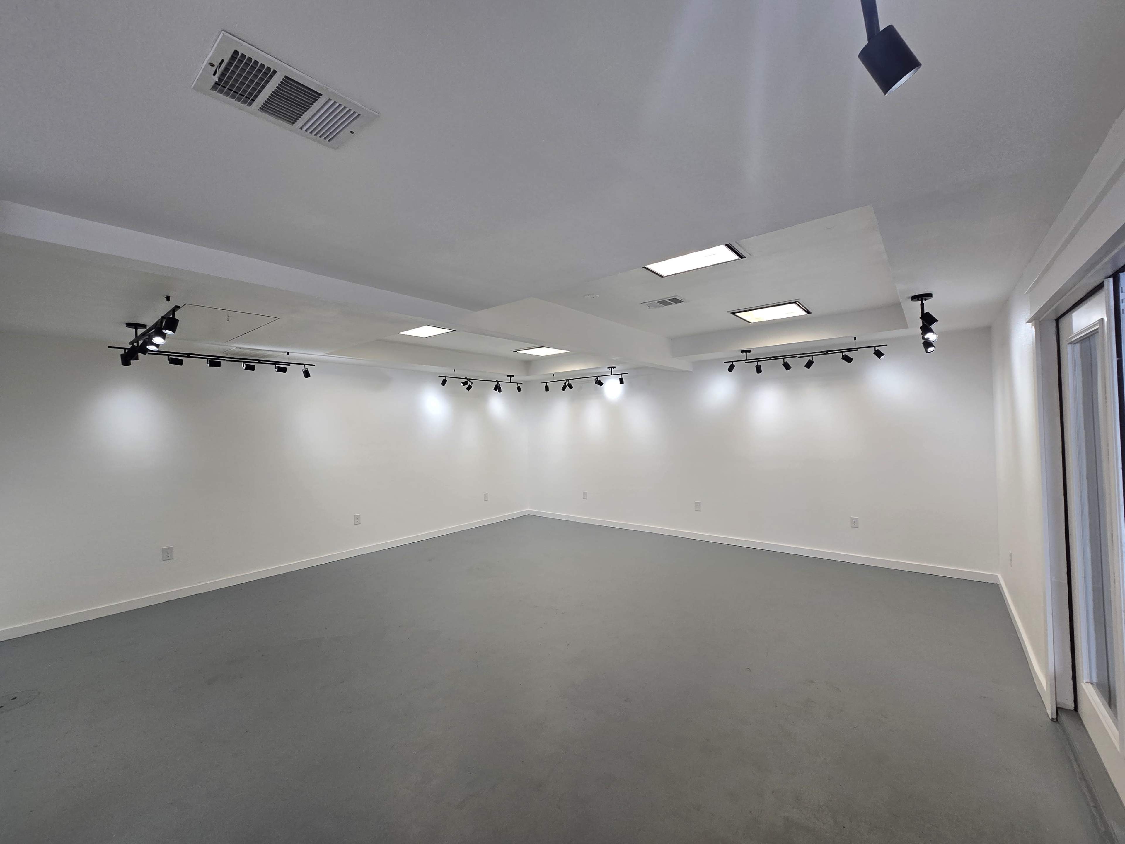 The image shows an empty, well-lit room with a gray floor and track lighting on the ceiling.
