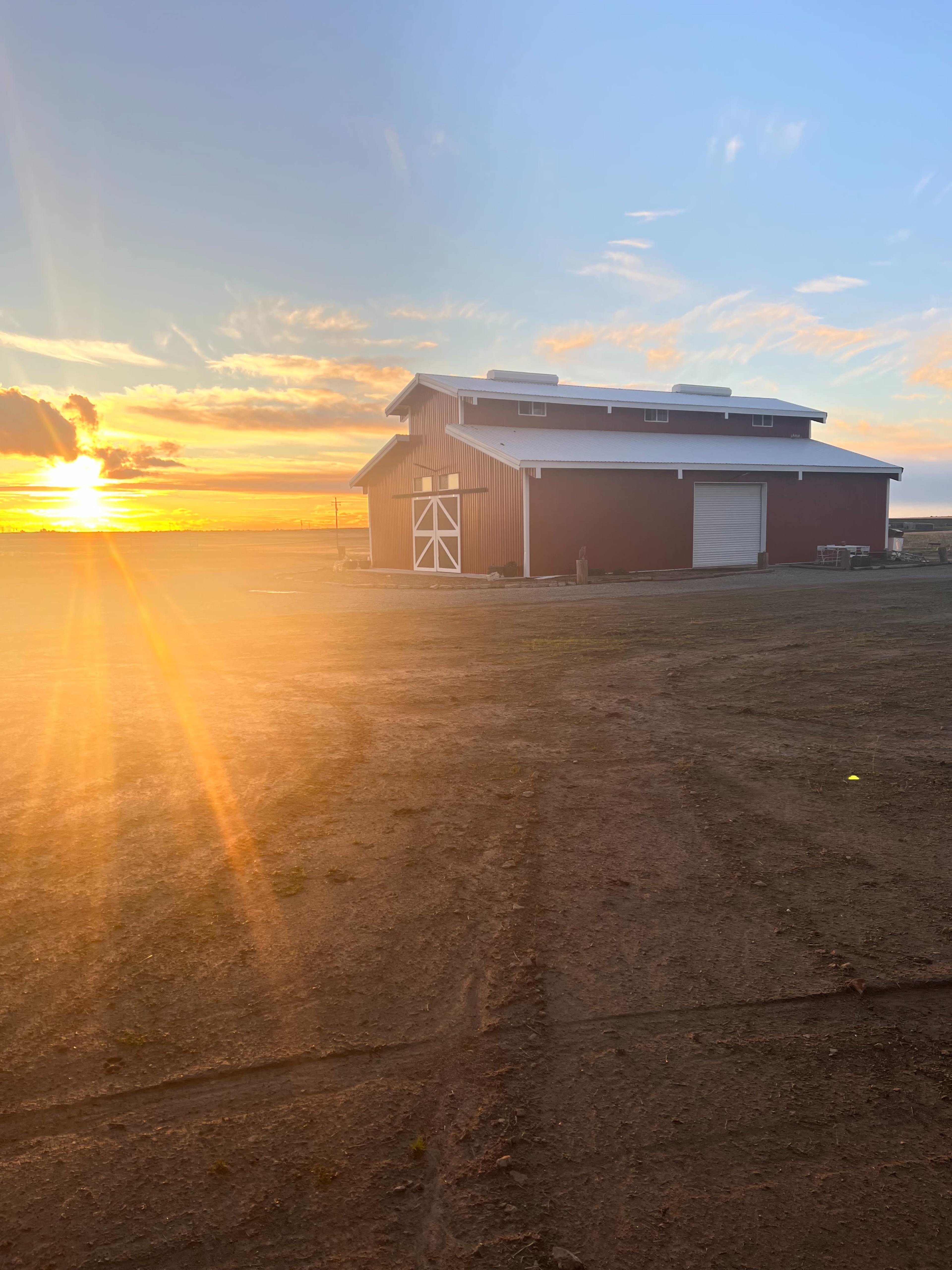 A red barn is positioned beside a dirt path under a sunset sky with vibrant clouds.