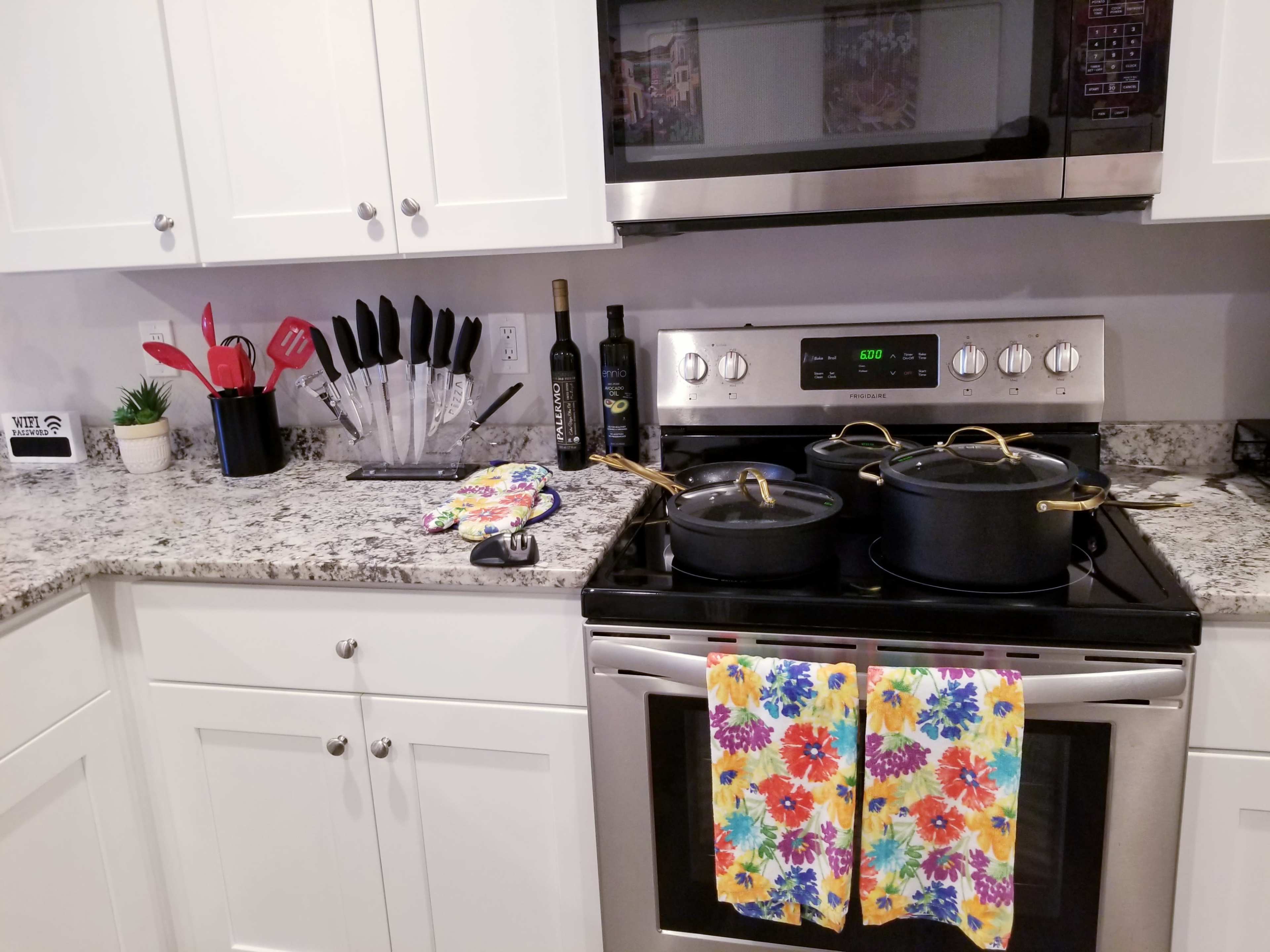 A kitchen countertop features a stove with two pots, colorful dish towels hanging in front, and a knife set neatly arranged in a holder nearby.