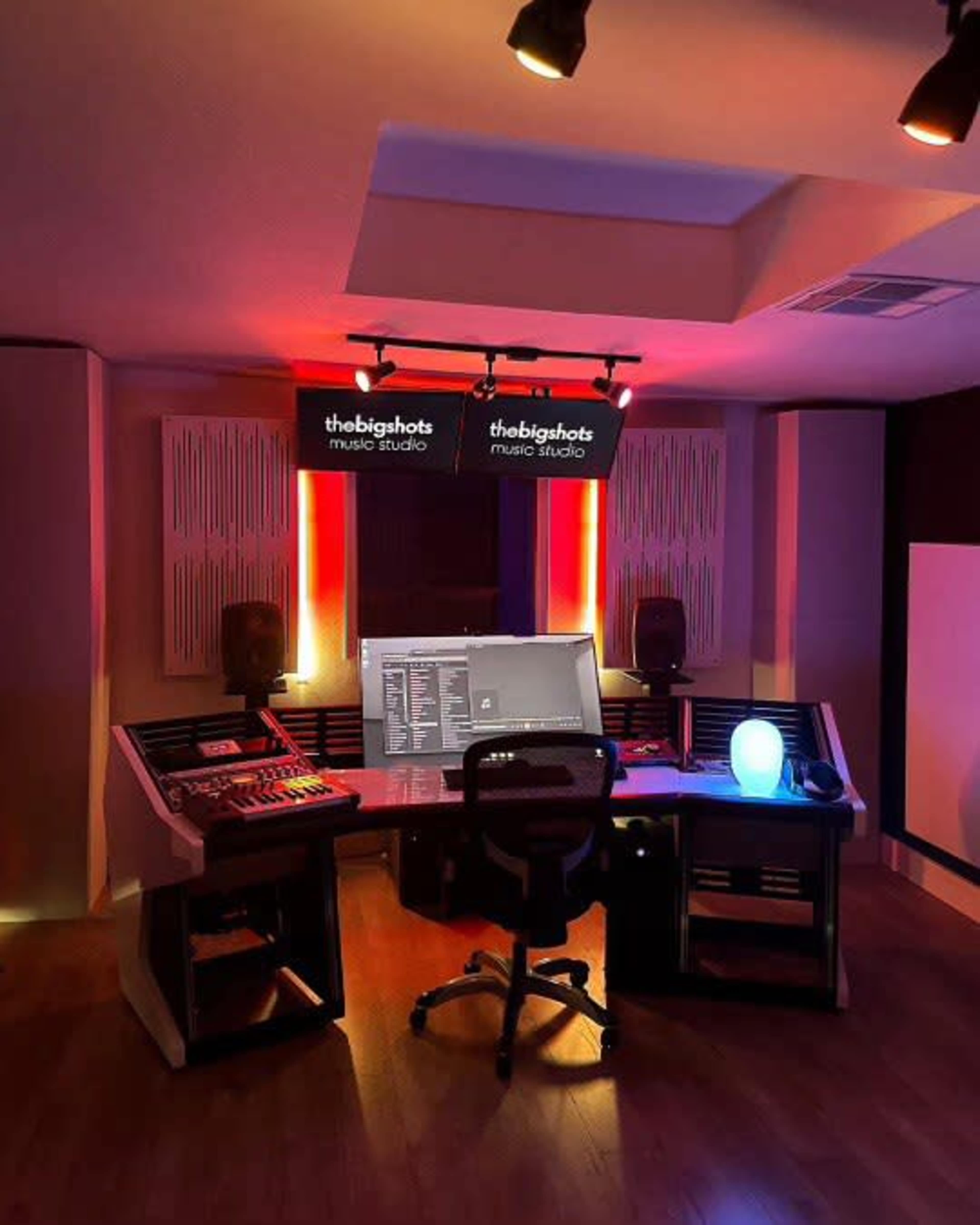 The image shows a modern music studio with a control desk, computer monitor, and ambient lighting.