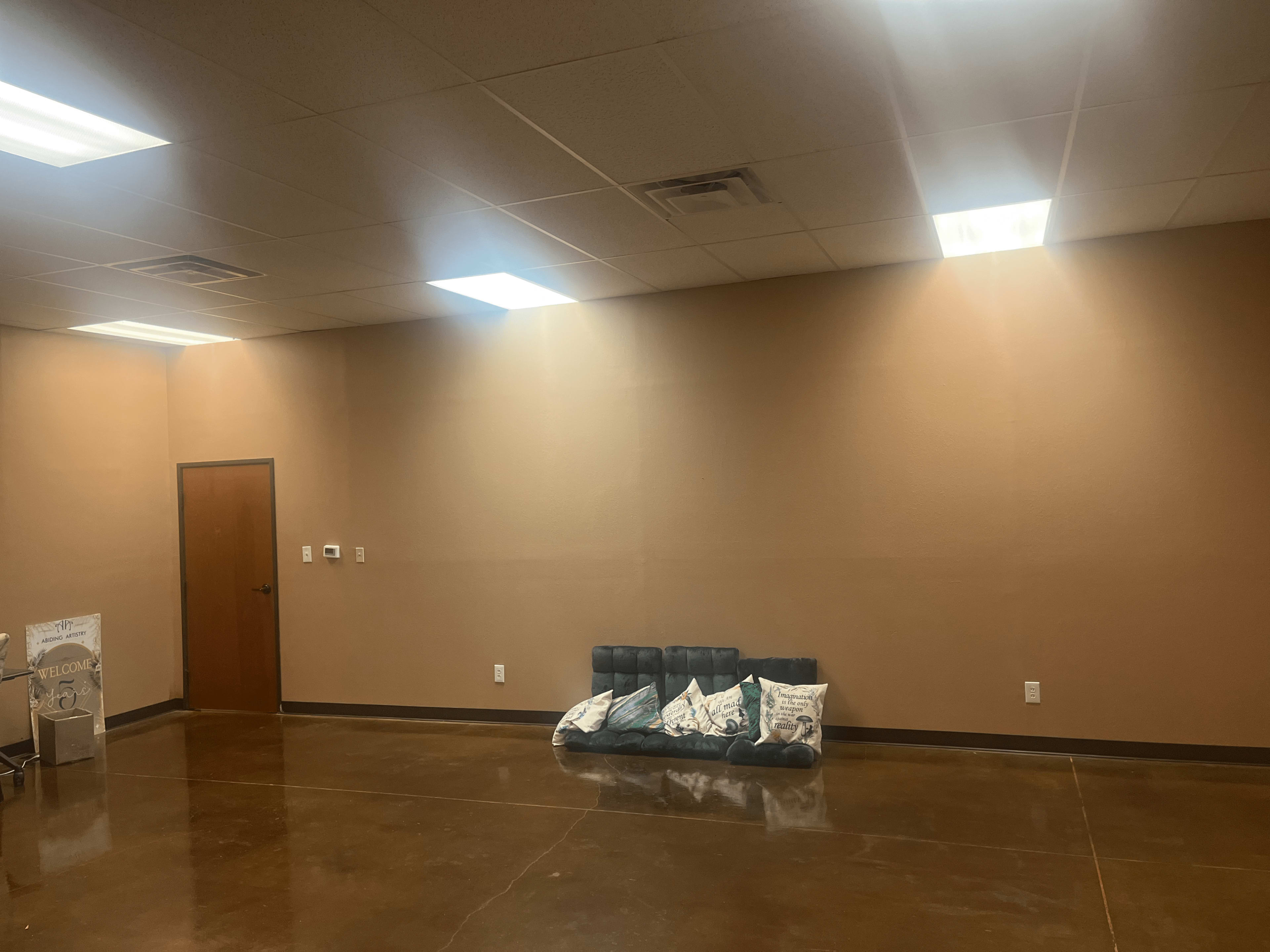 A sparsely furnished room with a brown-painted wall, a wooden door, and a low couch with pillows against one side.