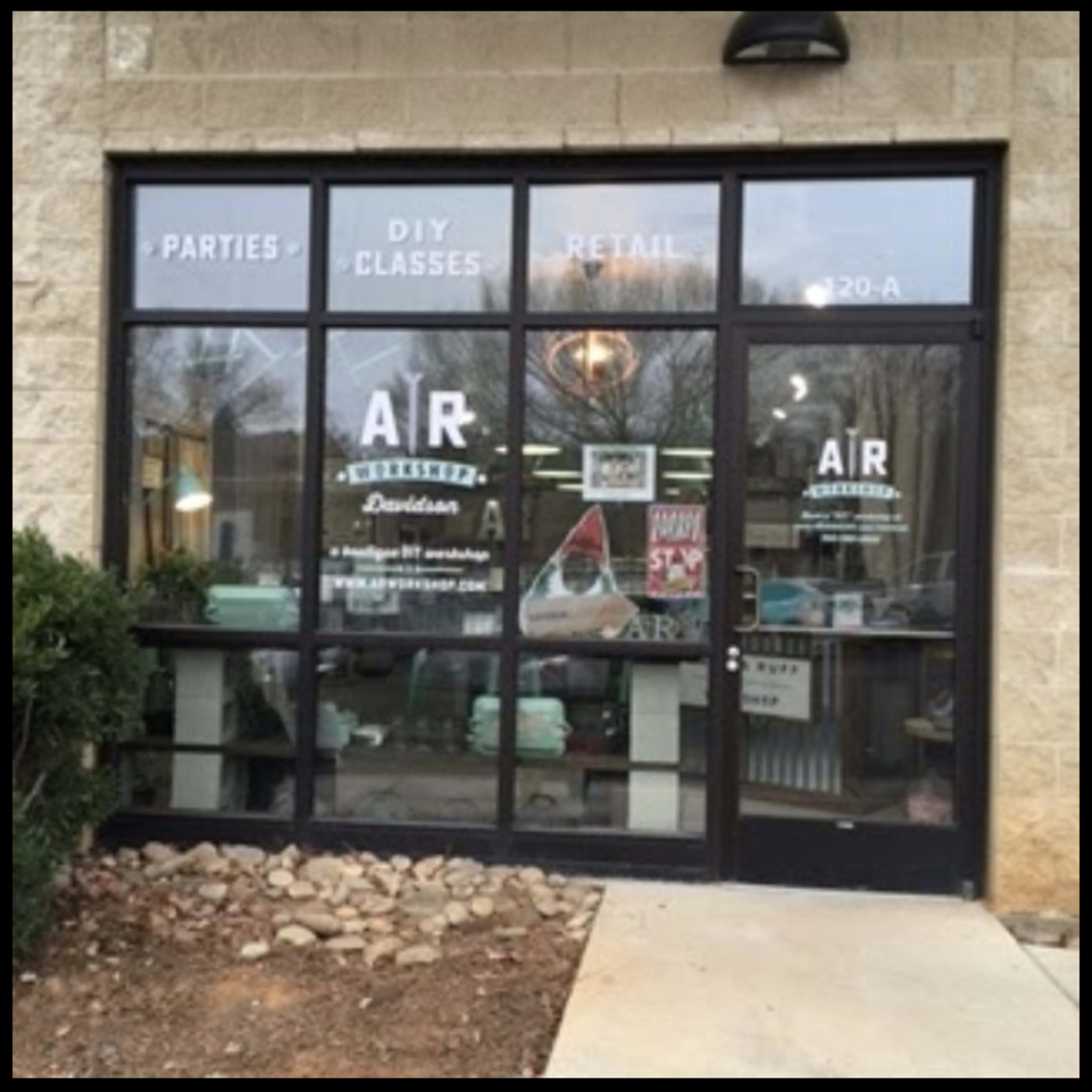 The entrance of a store with large glass windows displaying signage for parties, DIY classes, and retail items.