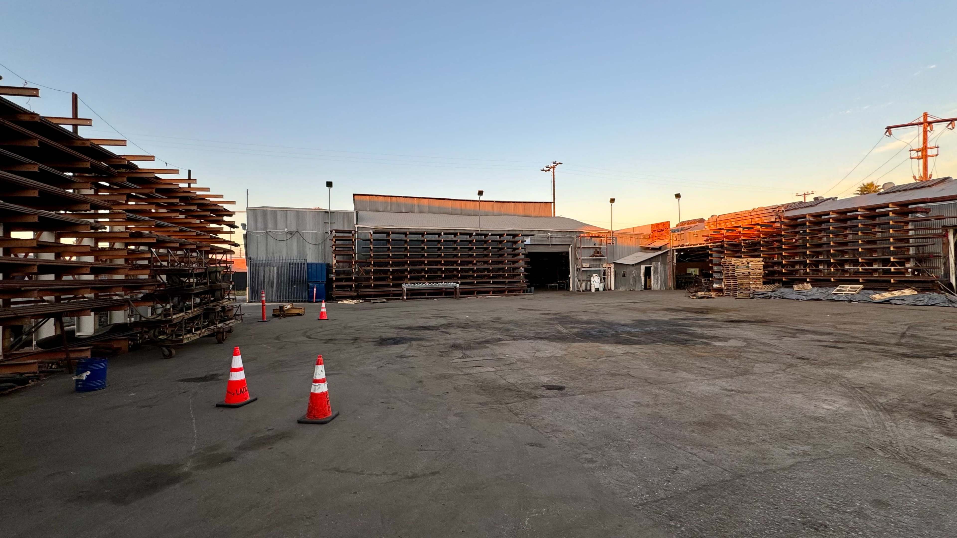 The image shows a large, empty industrial yard with stacks of wooden pallets on either side and construction cones arranged on the ground.