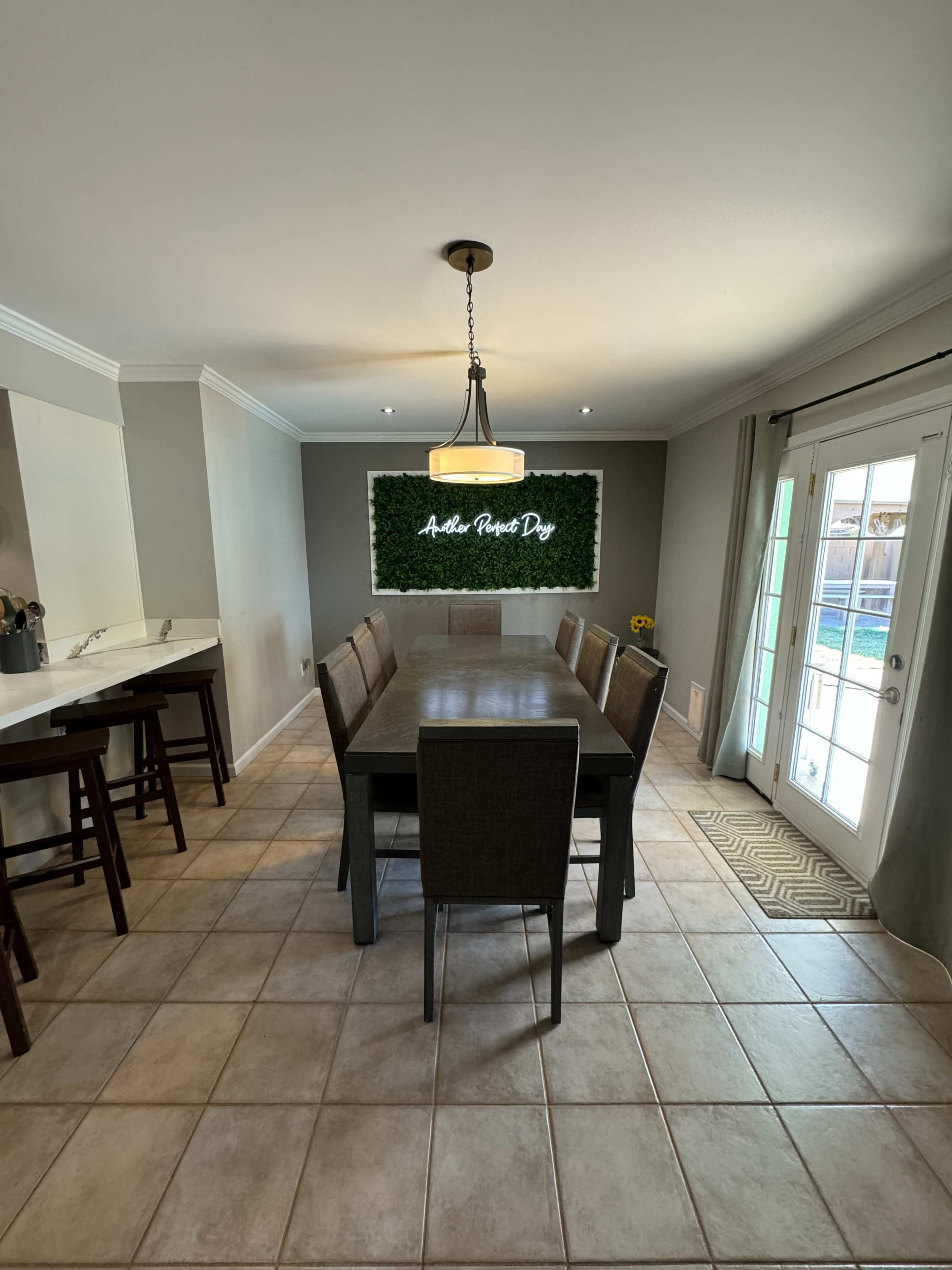 A dining area features a large rectangular table surrounded by chairs, with a decorative green wall and sliding glass doors leading outside.