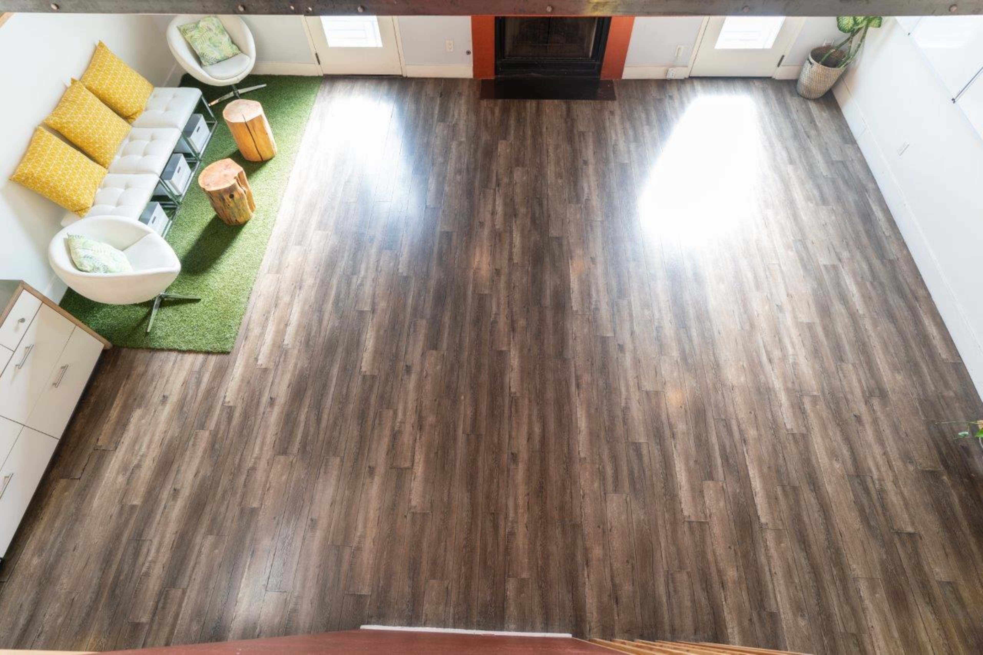 A spacious room features a seating area with a white couch and two chairs, a green rug, a fireplace, and wooden flooring.