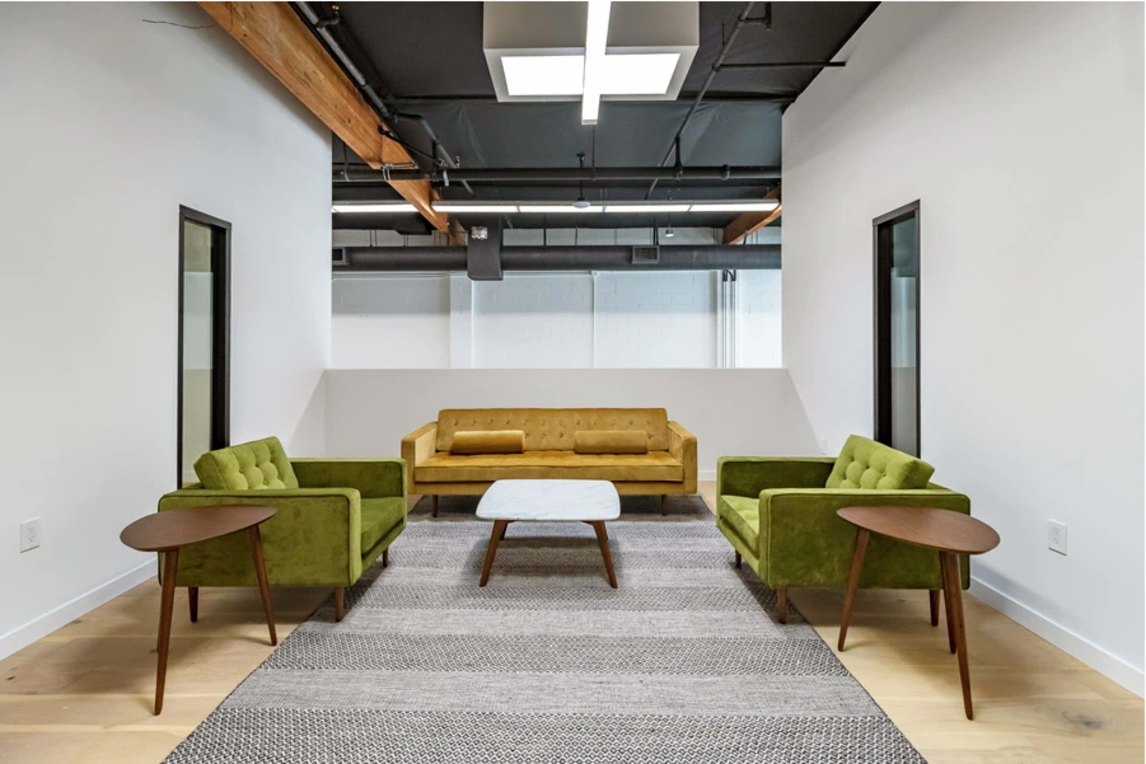 A modern, minimalistic lounge area featuring a yellow sofa, two green armchairs, a white coffee table, and a patterned rug on light wooden flooring.