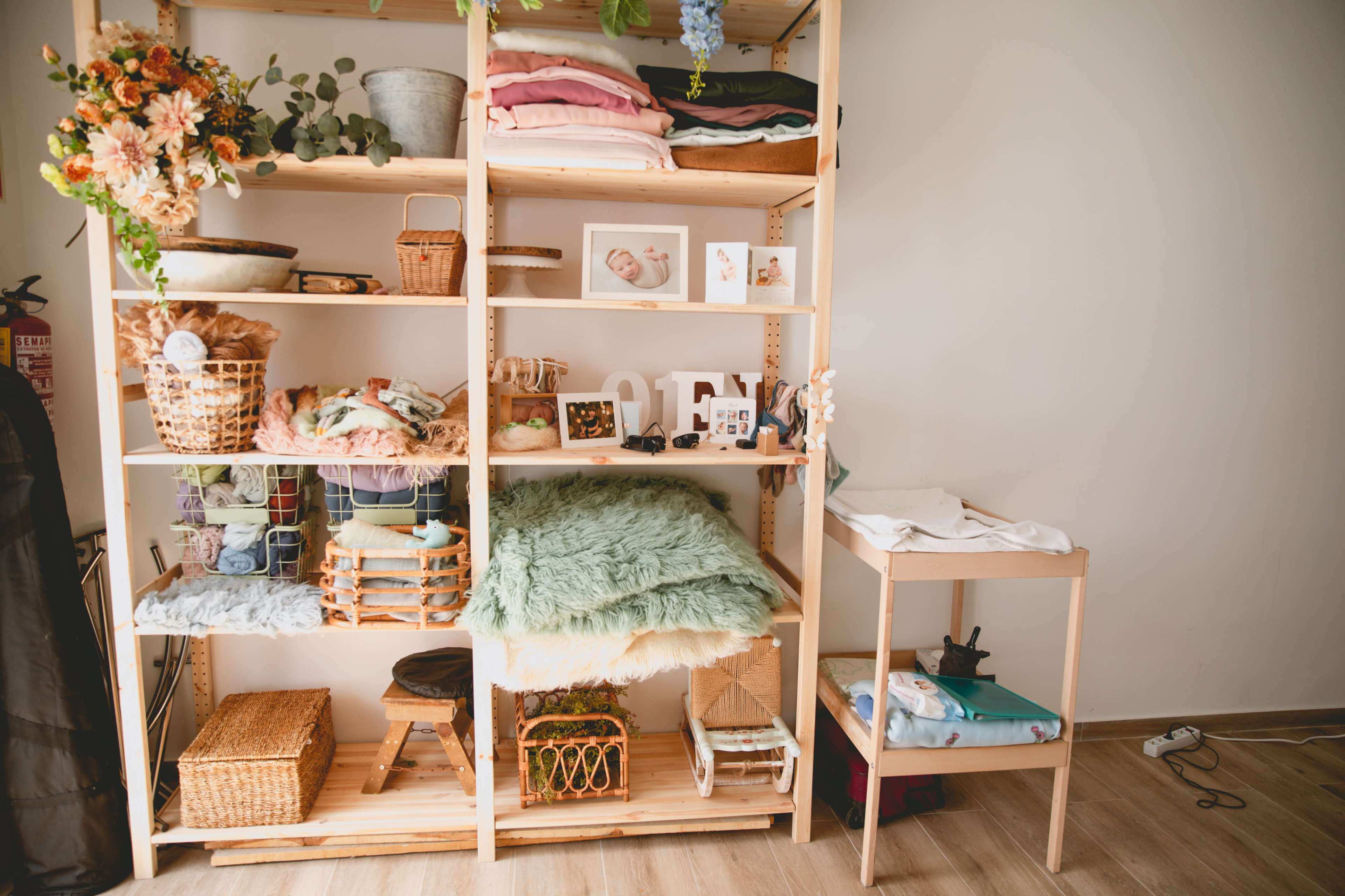 A wooden shelf filled with various items, including textiles, baskets, and decorative elements, alongside a small table with additional supplies.