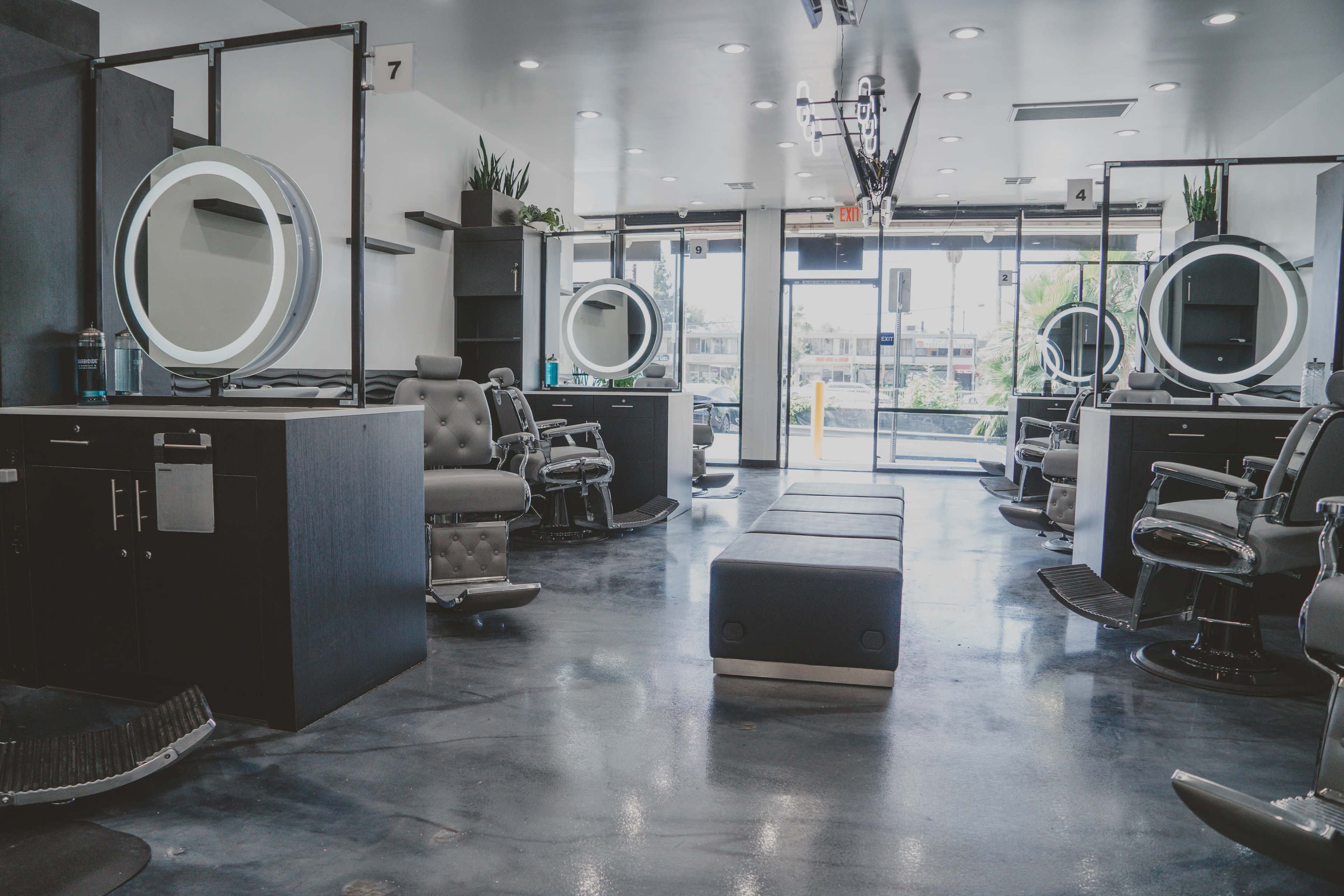 A modern barber shop with several styling stations equipped with round mirrors, black chairs, and large windows allowing natural light to enter.