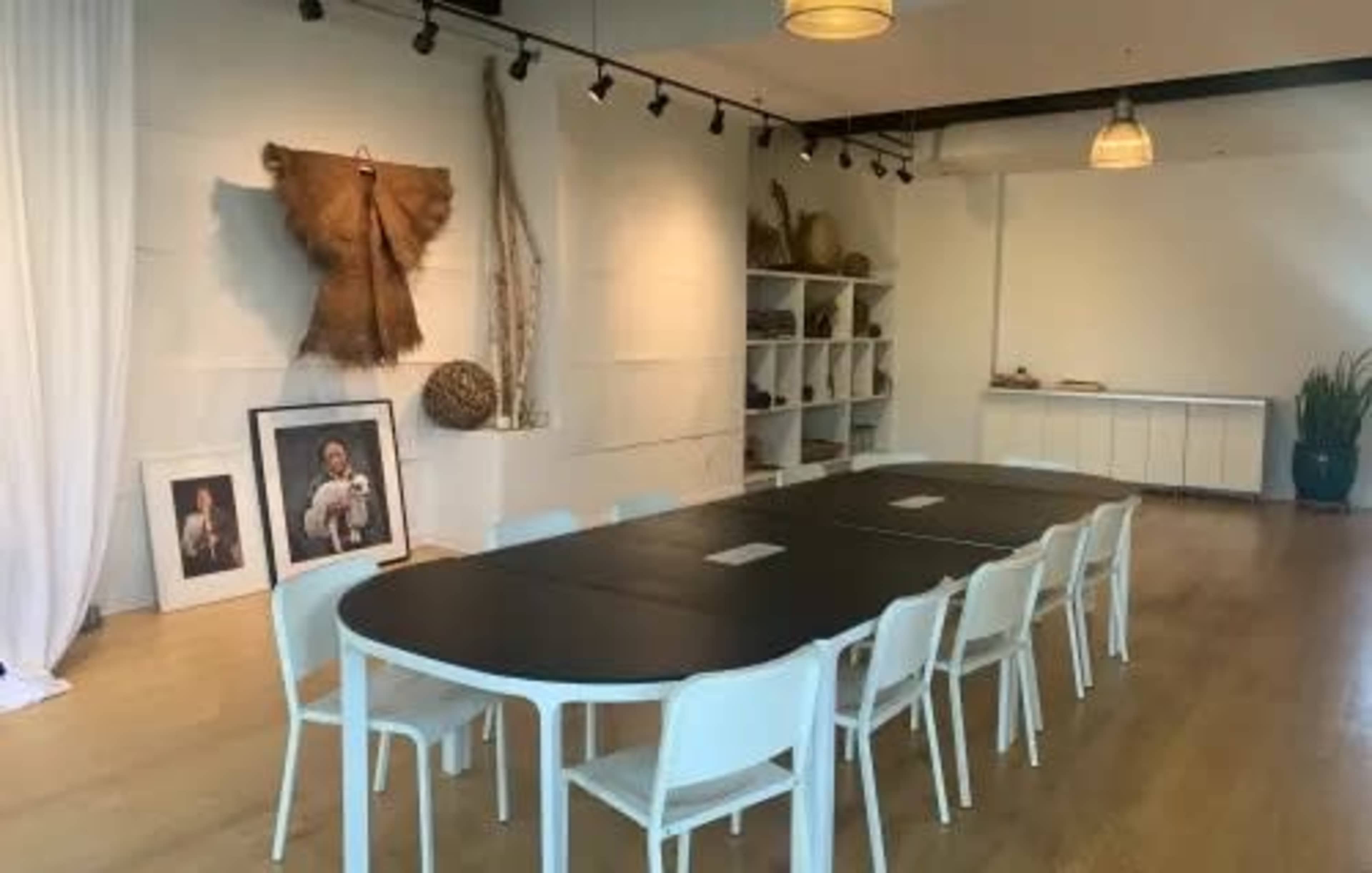 A spacious meeting room with a long black table surrounded by white chairs, adorned with wall art and natural decor.
