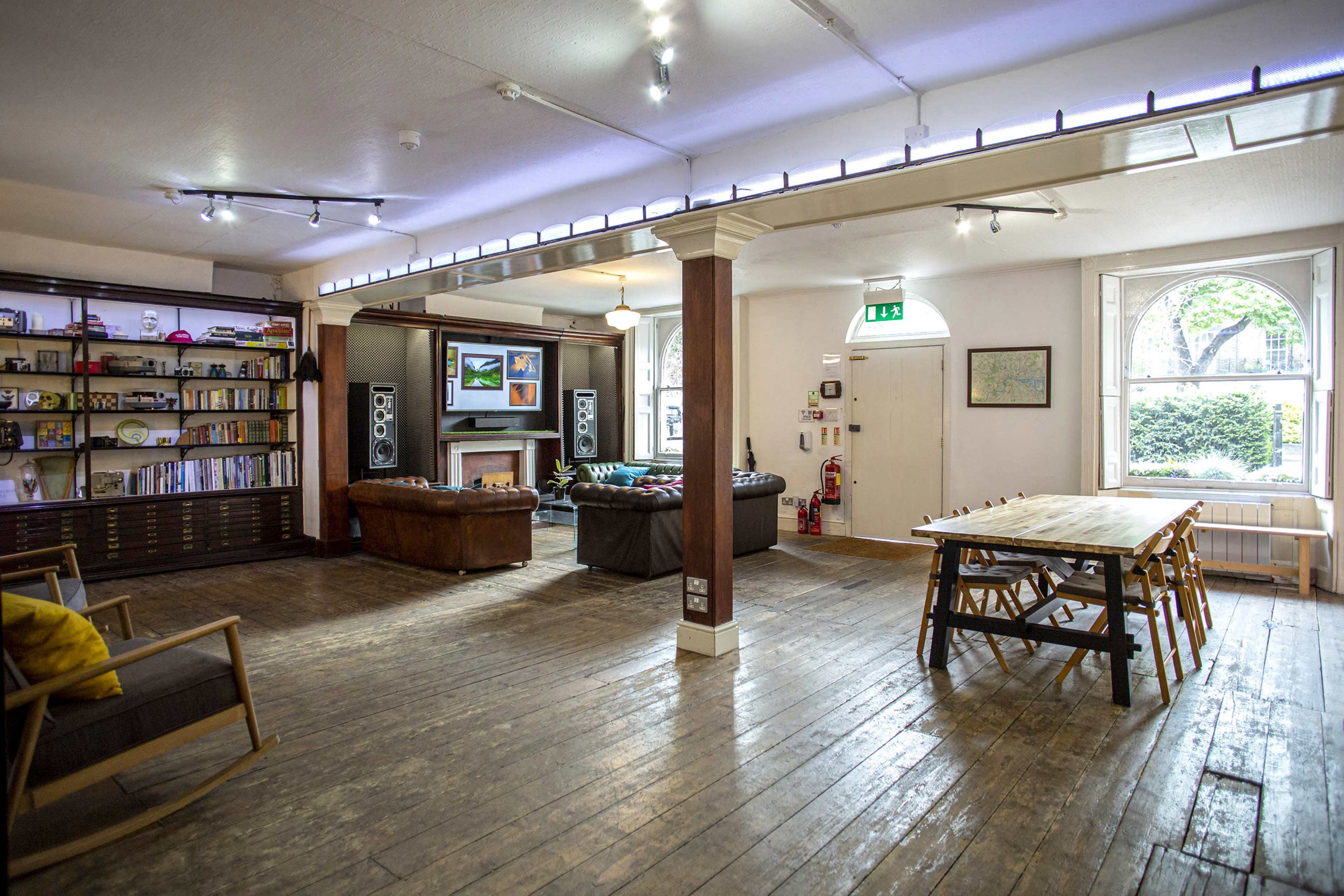 A spacious room with wooden floors, a large dining table, a couch, bookshelves, and a television mounted on the wall.