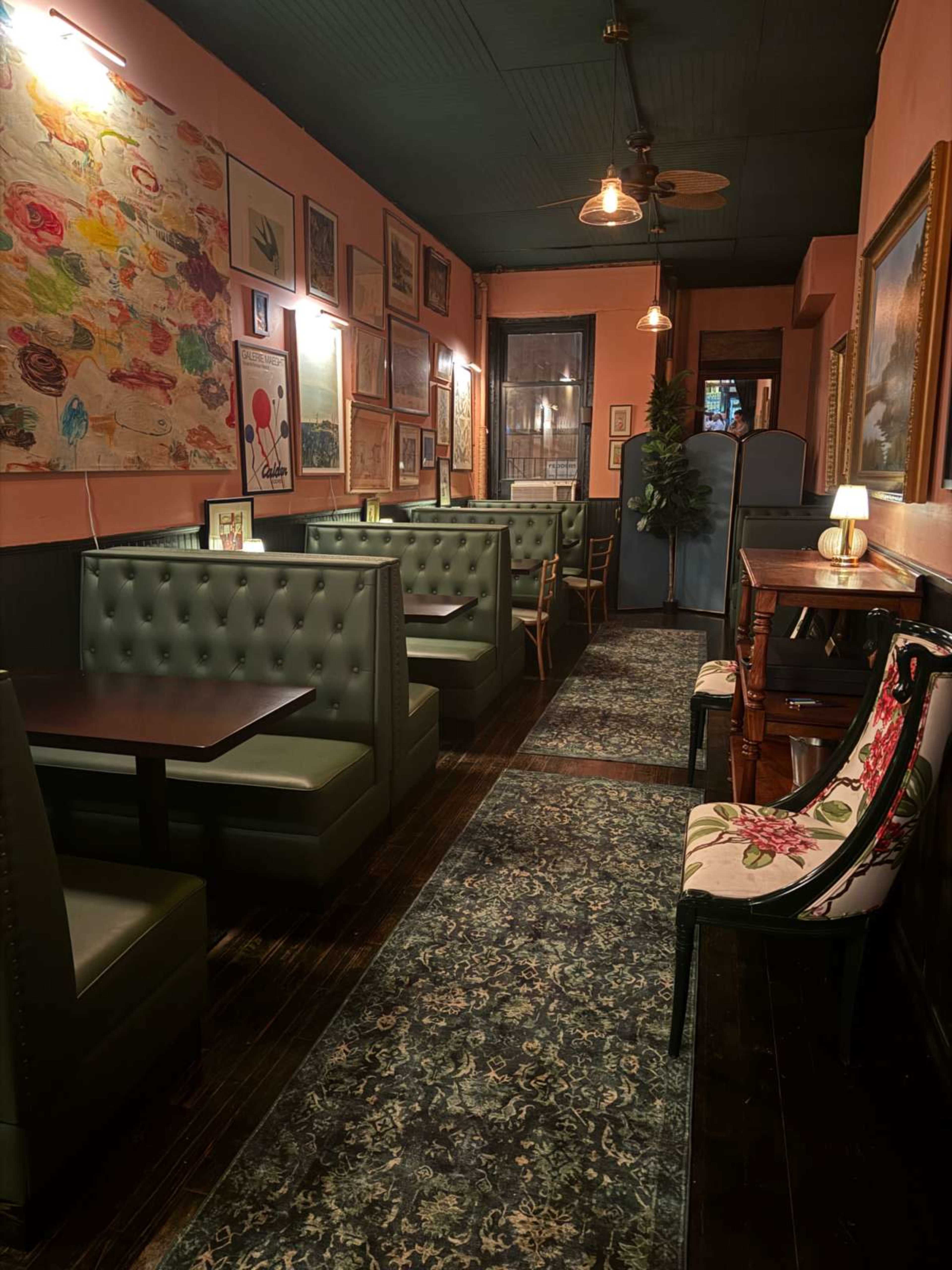 The image depicts a narrow restaurant interior with green upholstered booths along the walls, framed artwork, and warm lighting.