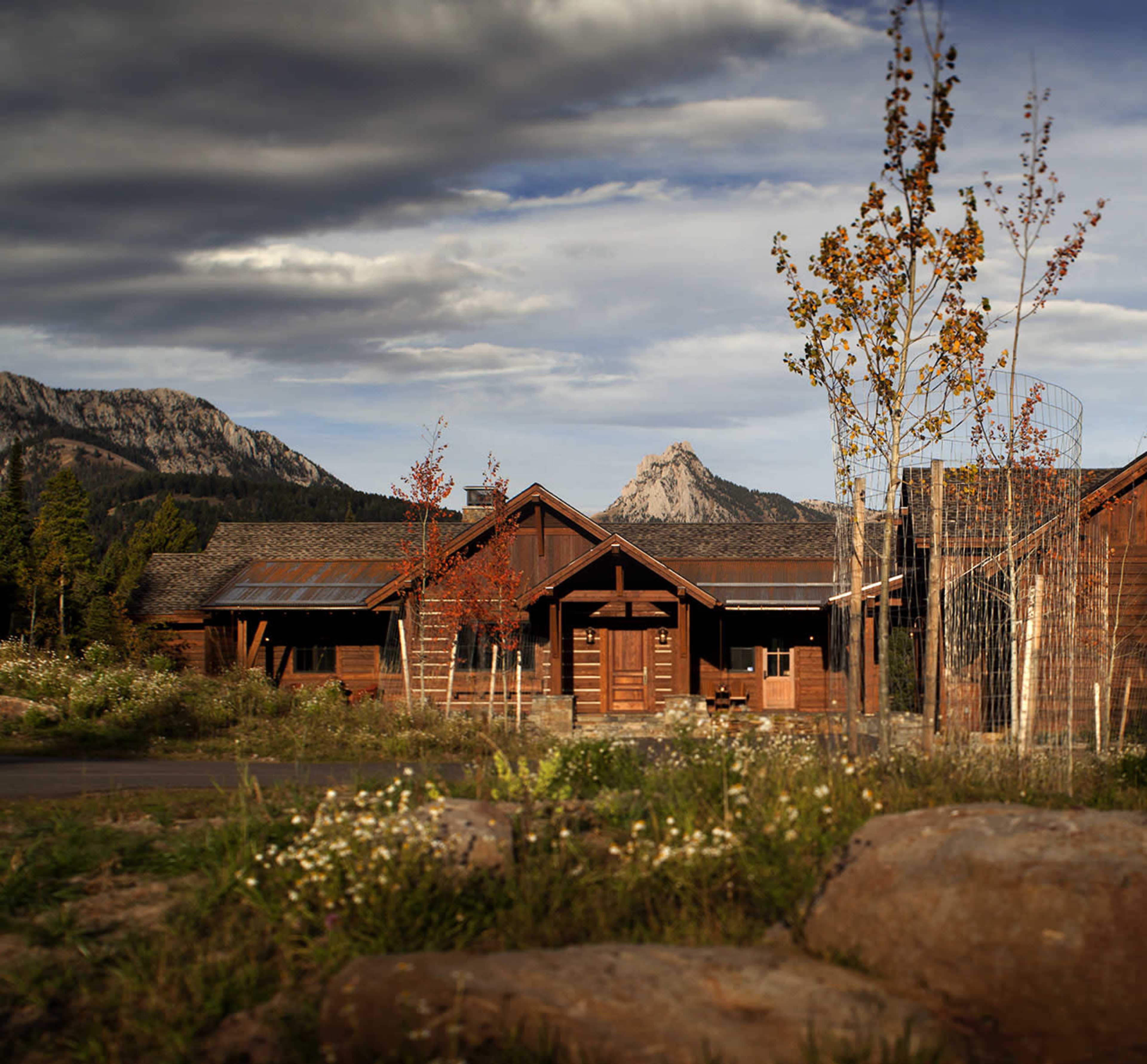 A wooden cabin surrounded by trees and mountains under a cloudy sky.