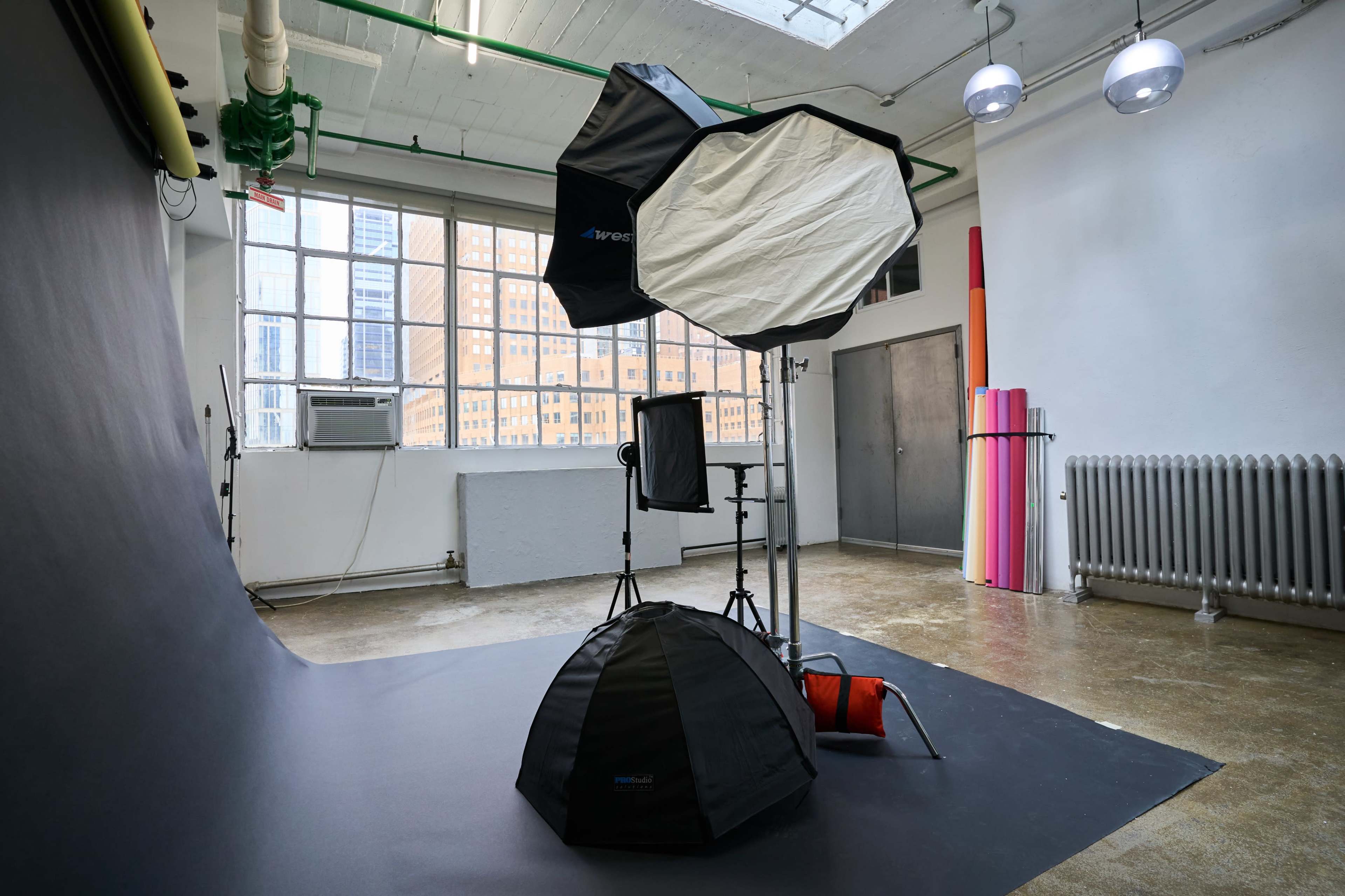 A photography studio setup with softbox lights, a backdrop, and various equipment against a white wall and large windows.