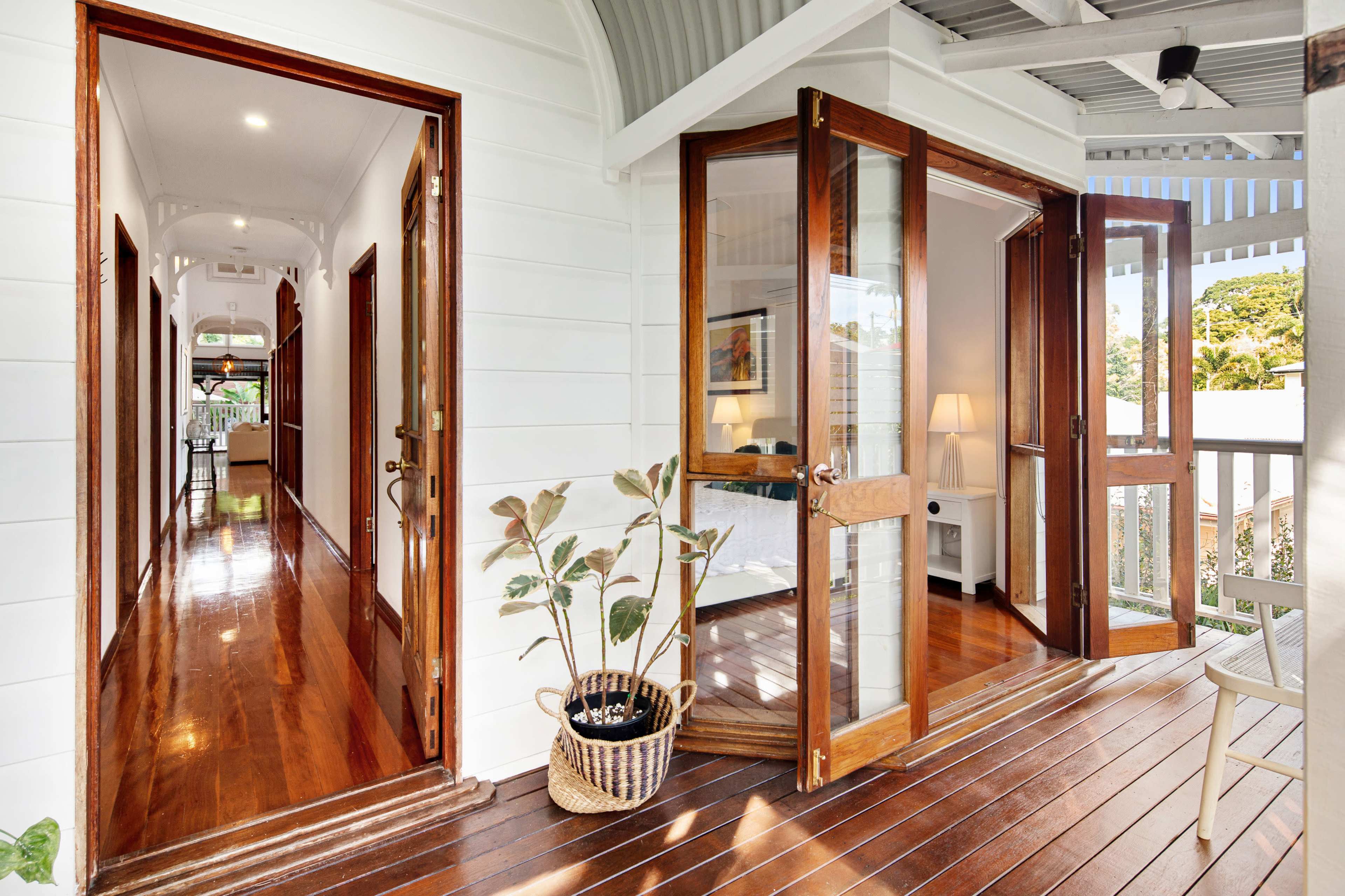 A wooden veranda with two sets of double glass doors leading into a bright interior and a hallway extending to the left.