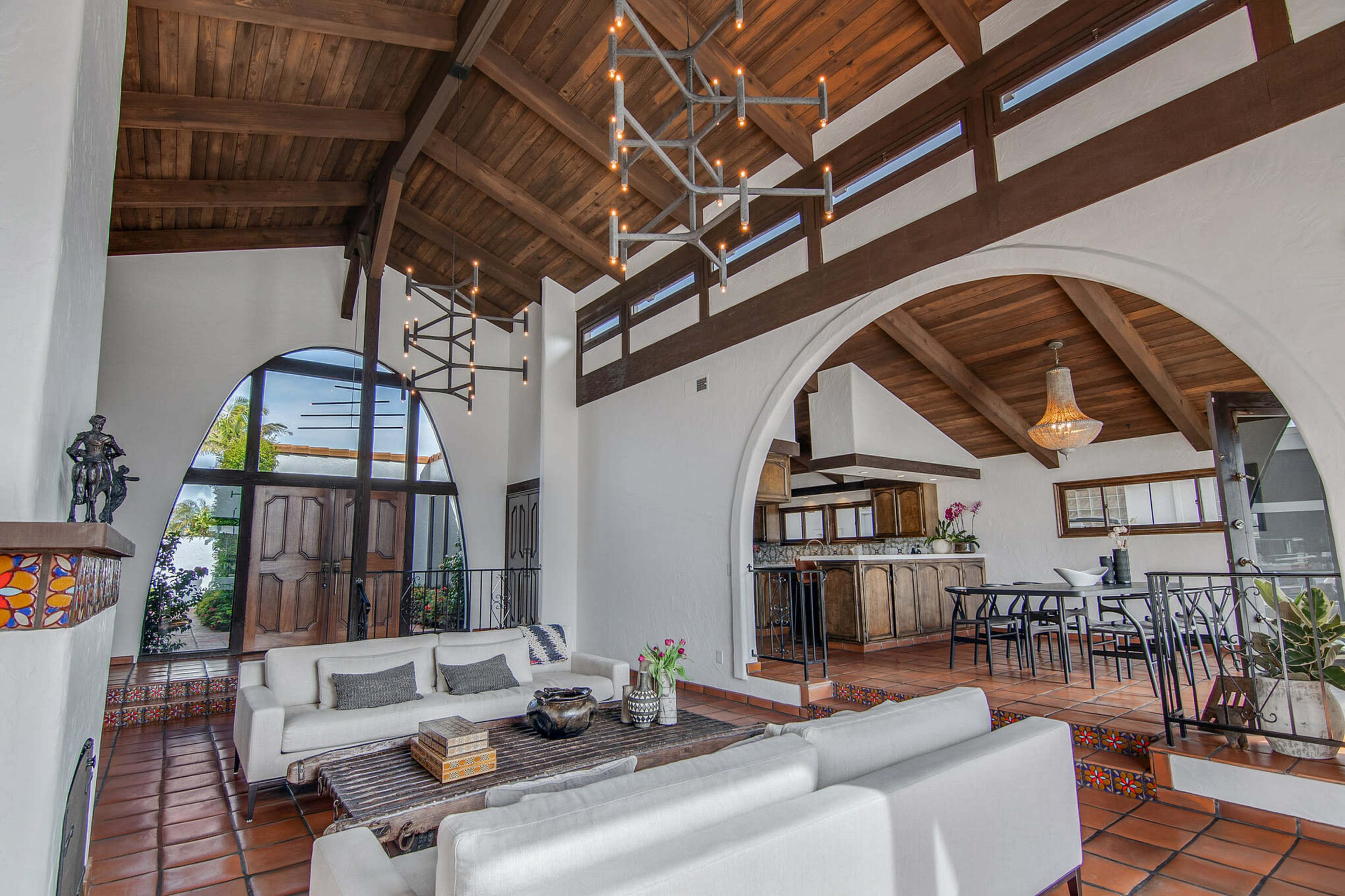 The interior features a spacious, open-concept living area with high wooden ceilings, an arched entryway, and a mix of modern and rustic decor.