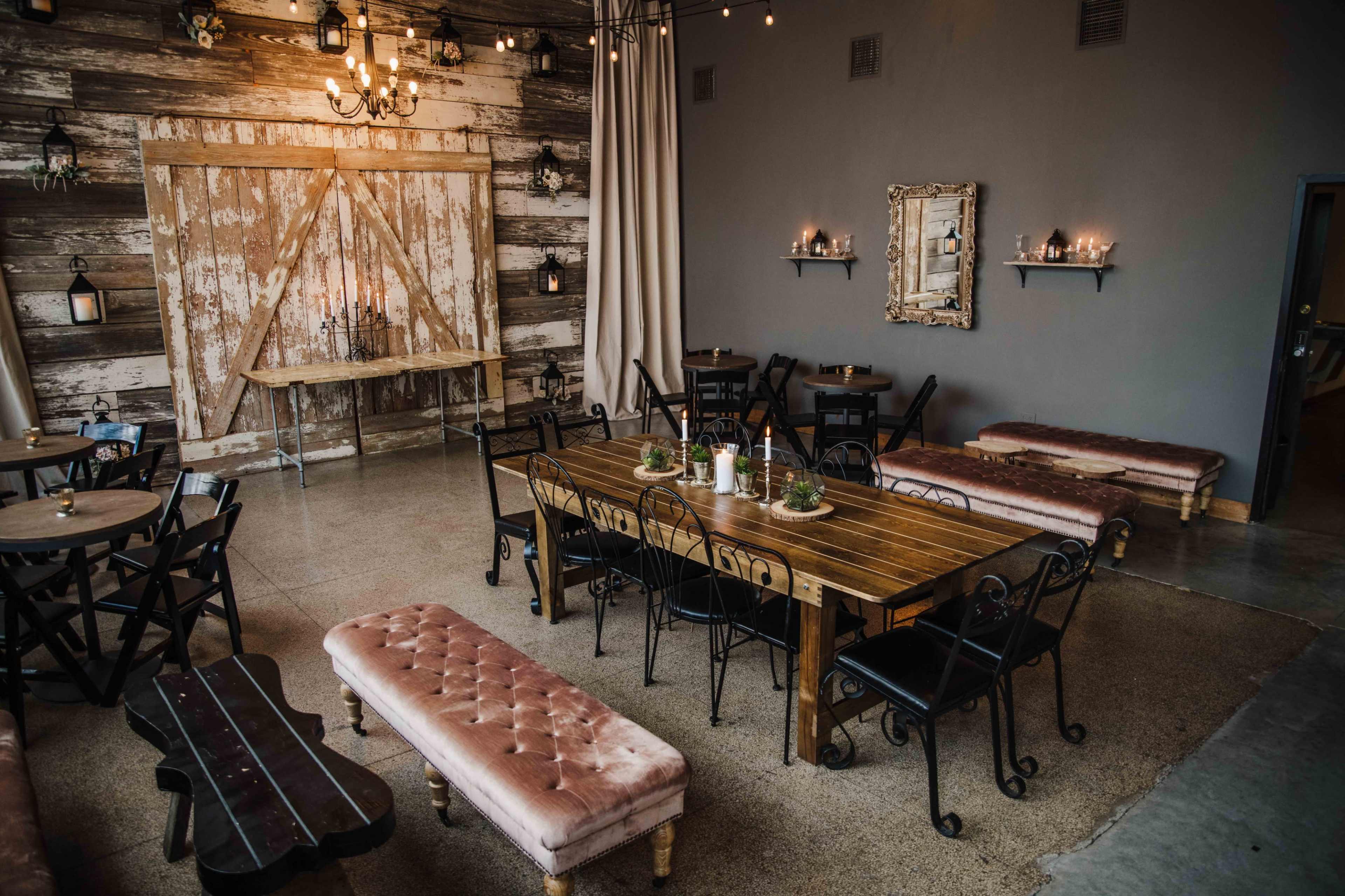 A rustic dining area with a large wooden table, several smaller tables, and benches, all arranged beneath warm lighting and decorative wall features.
