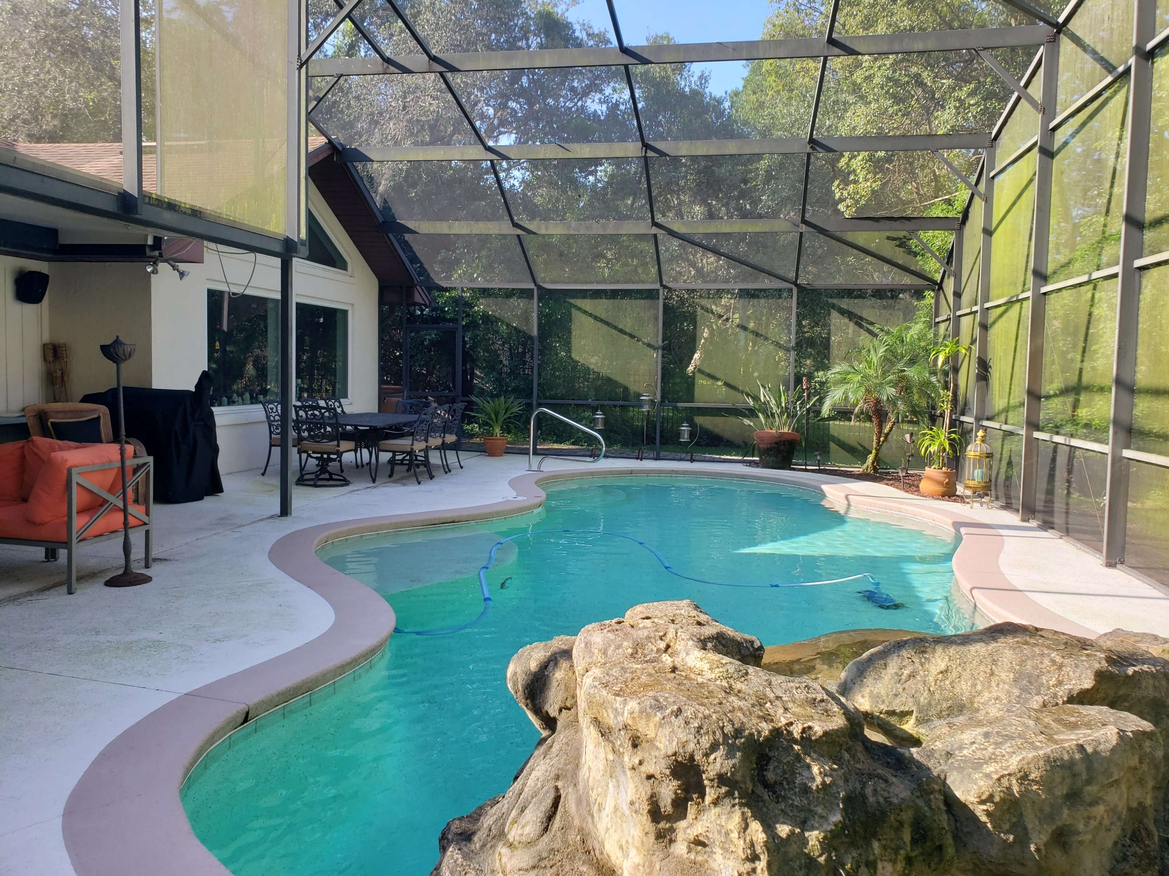 A screened-in pool area featuring a curved swimming pool with a rock formation and adjacent seating space.