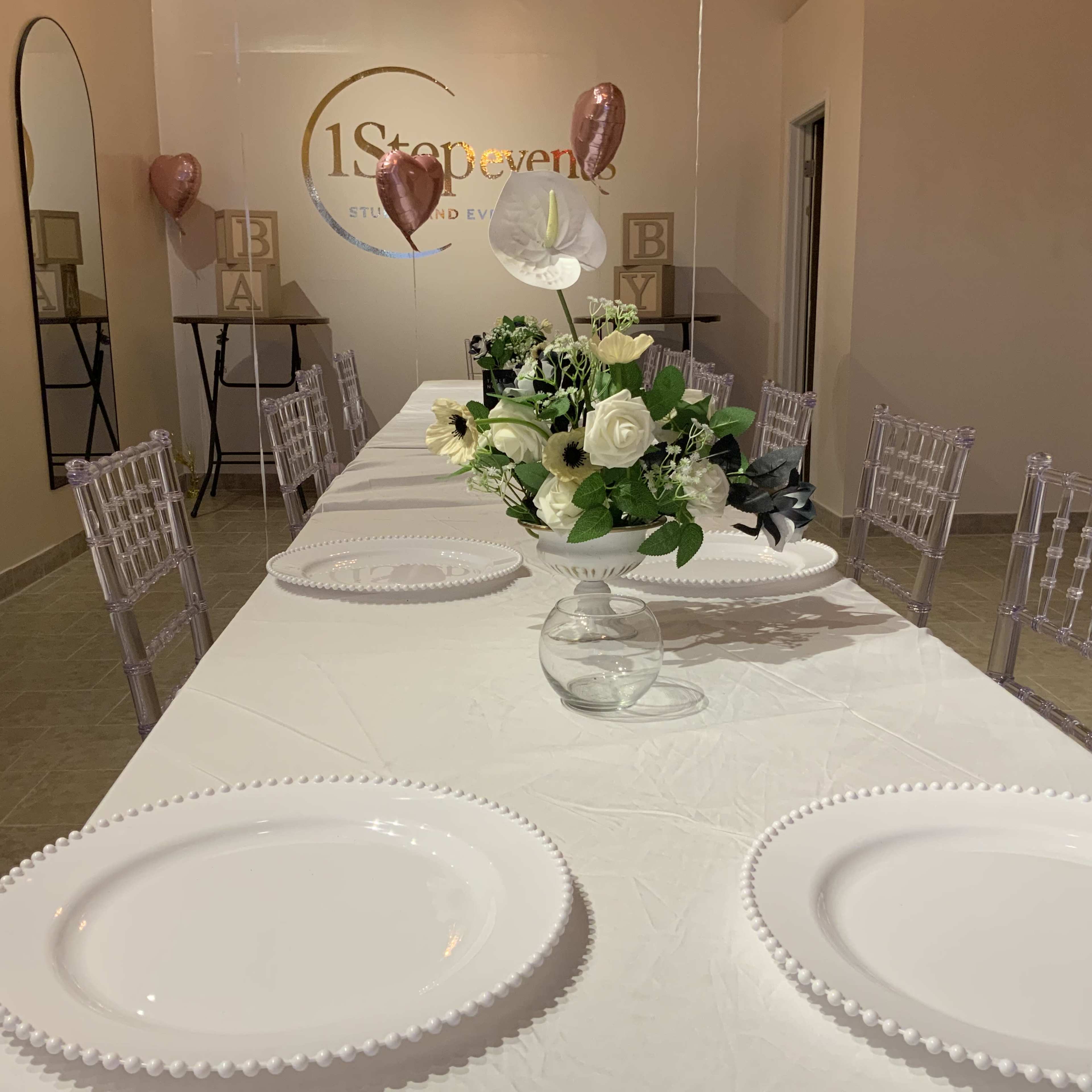The image shows a decorated banquet table with white plates, a floral centerpiece, and two pink balloons on either side in a well-lit event space.