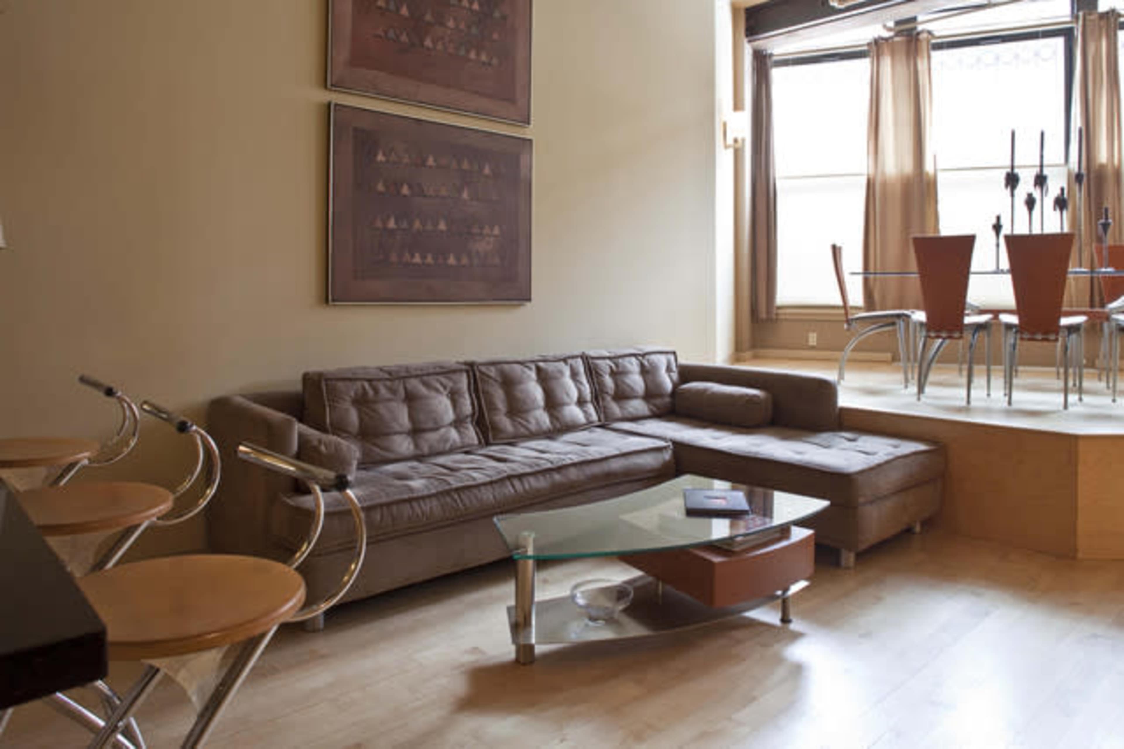 A modern living room with a brown sectional sofa, a glass coffee table, and a dining area featuring a round table and four chairs.