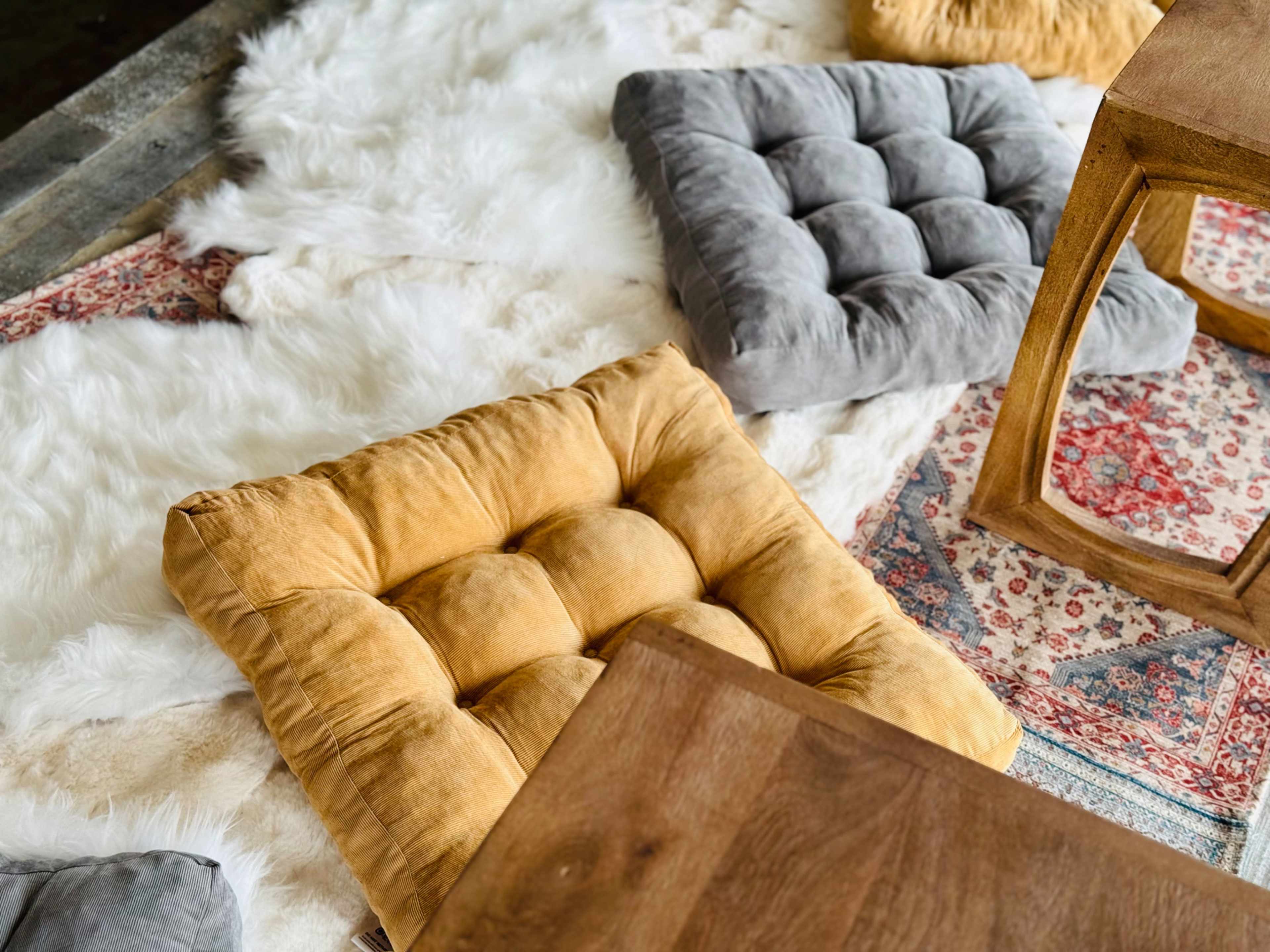 A living space with several cushioned floor pillows on a textured rug, accompanied by a wooden table.