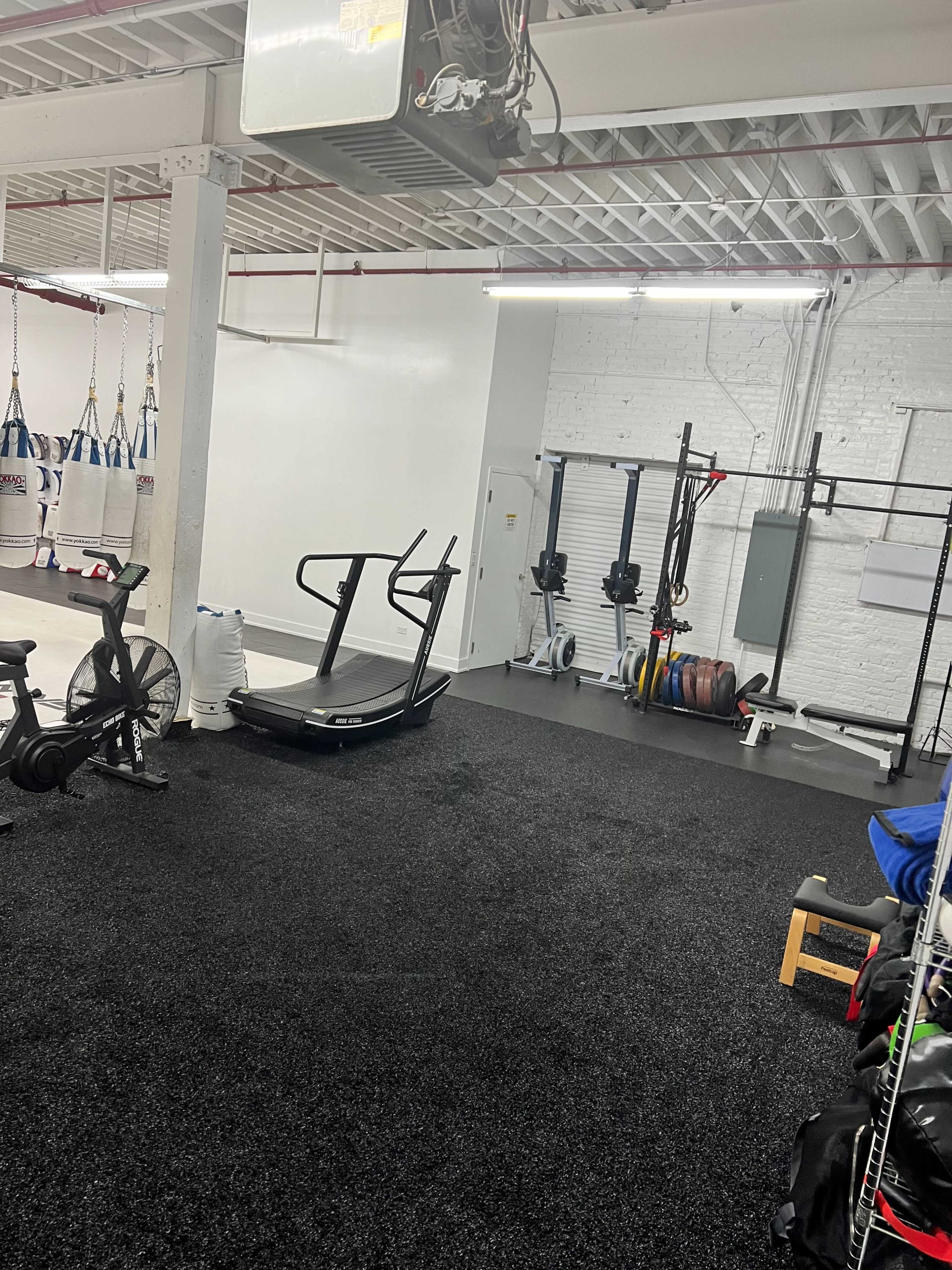 A fitness gym with exercise equipment, including a treadmill and weights, situated on a rubber flooring surface.