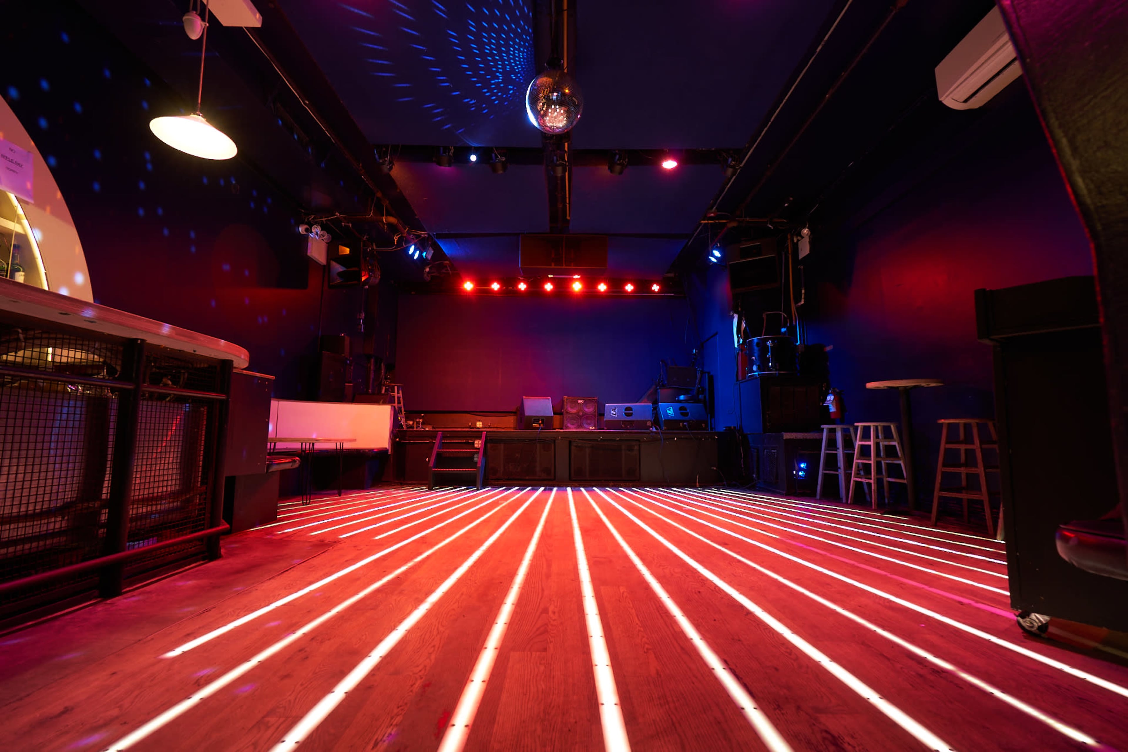 A dimly lit dance floor with streaks of light and a disco ball hanging from the ceiling in a music venue.