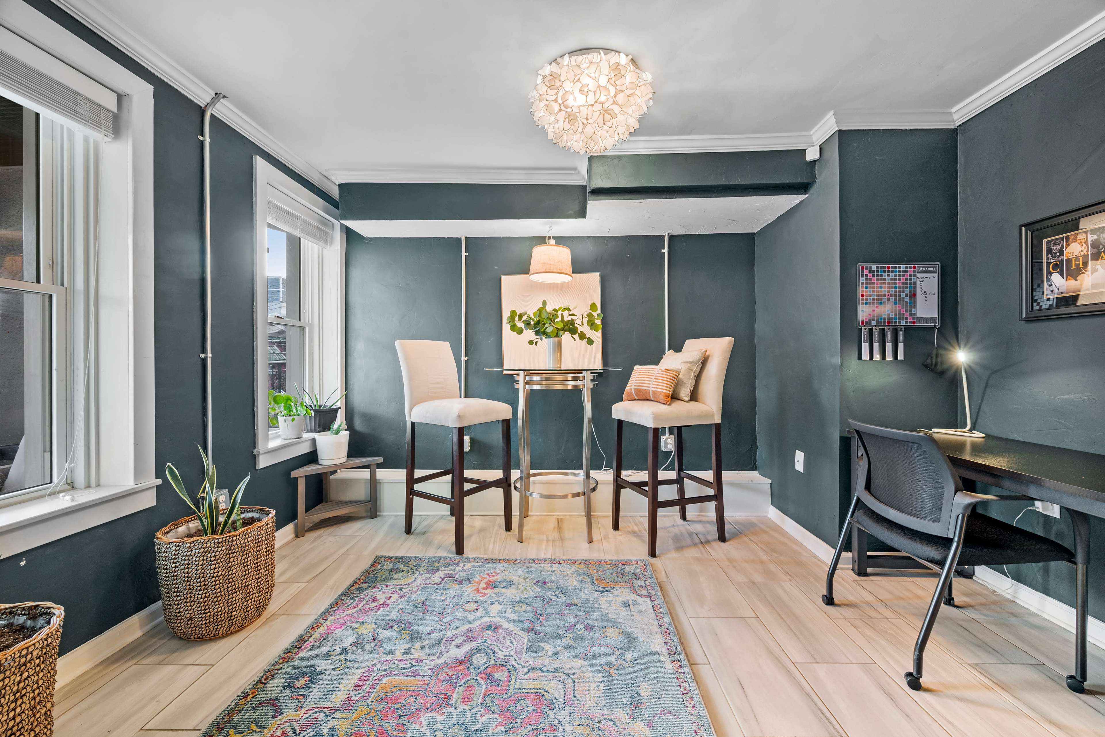 A small dining area with two tall chairs at a round table, surrounded by green walls and featuring a decorative light fixture above.