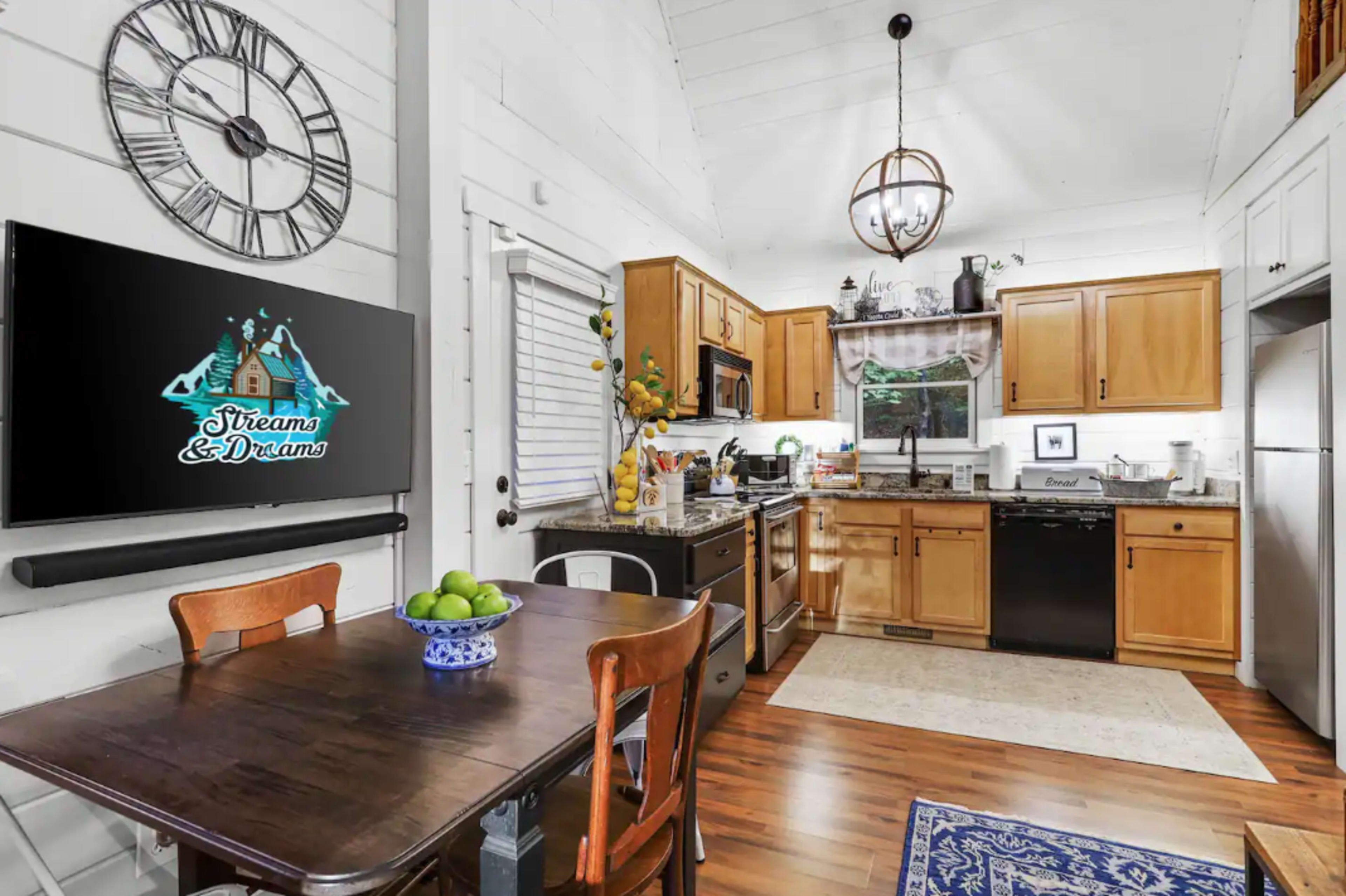 A kitchen with wooden cabinetry, a dining table, and a television mounted on the wall displaying a logo.