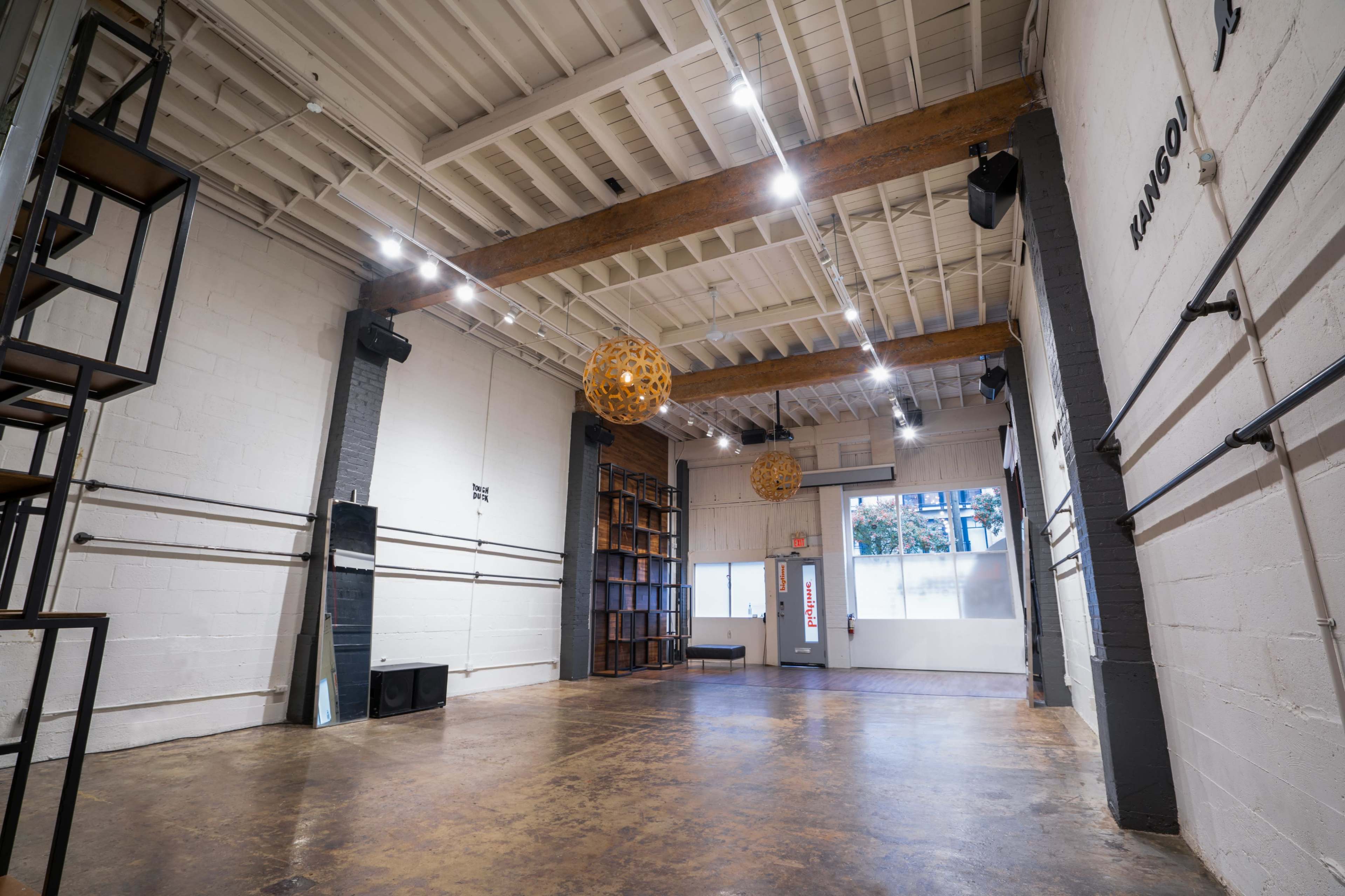 An empty room with wooden beams, track lighting, a large bookshelf, and two round pendant lights hanging from the ceiling.