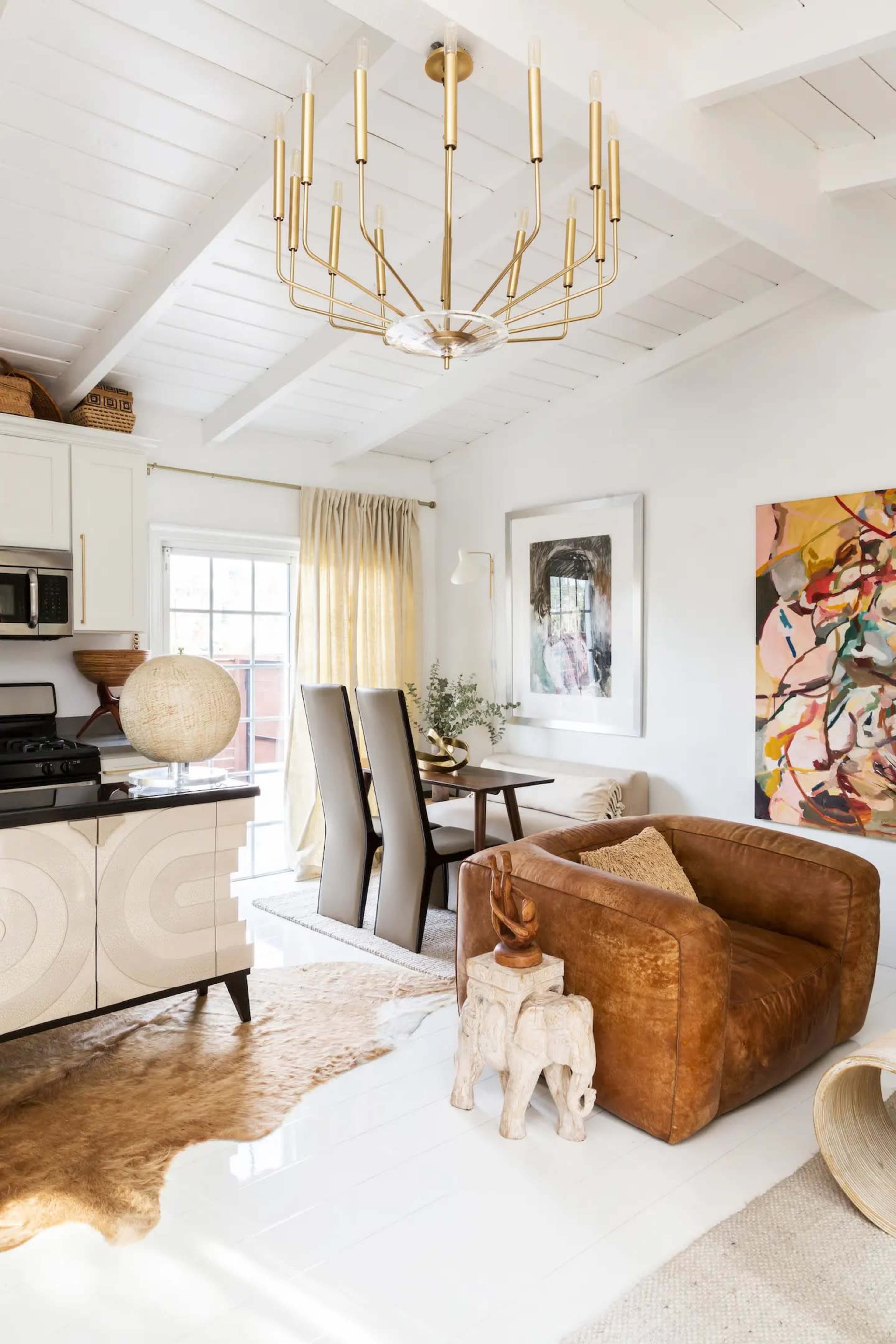 A stylish living space with a brown armchair, a dining table set, a patterned area rug, and artwork on the walls.