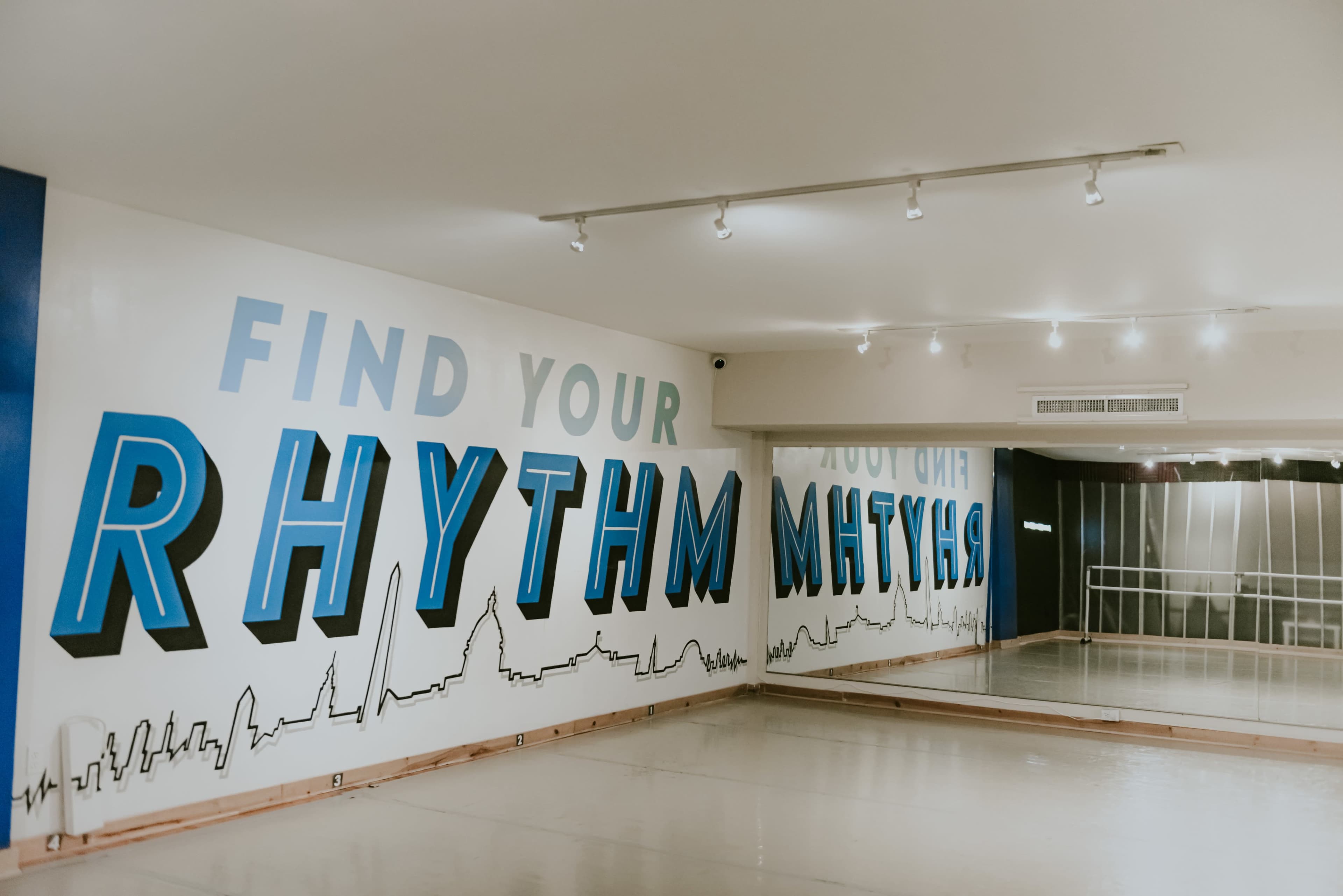 A spacious dance studio with a wall featuring the phrase "FIND YOUR RHYTHM" in bold blue and black letters.