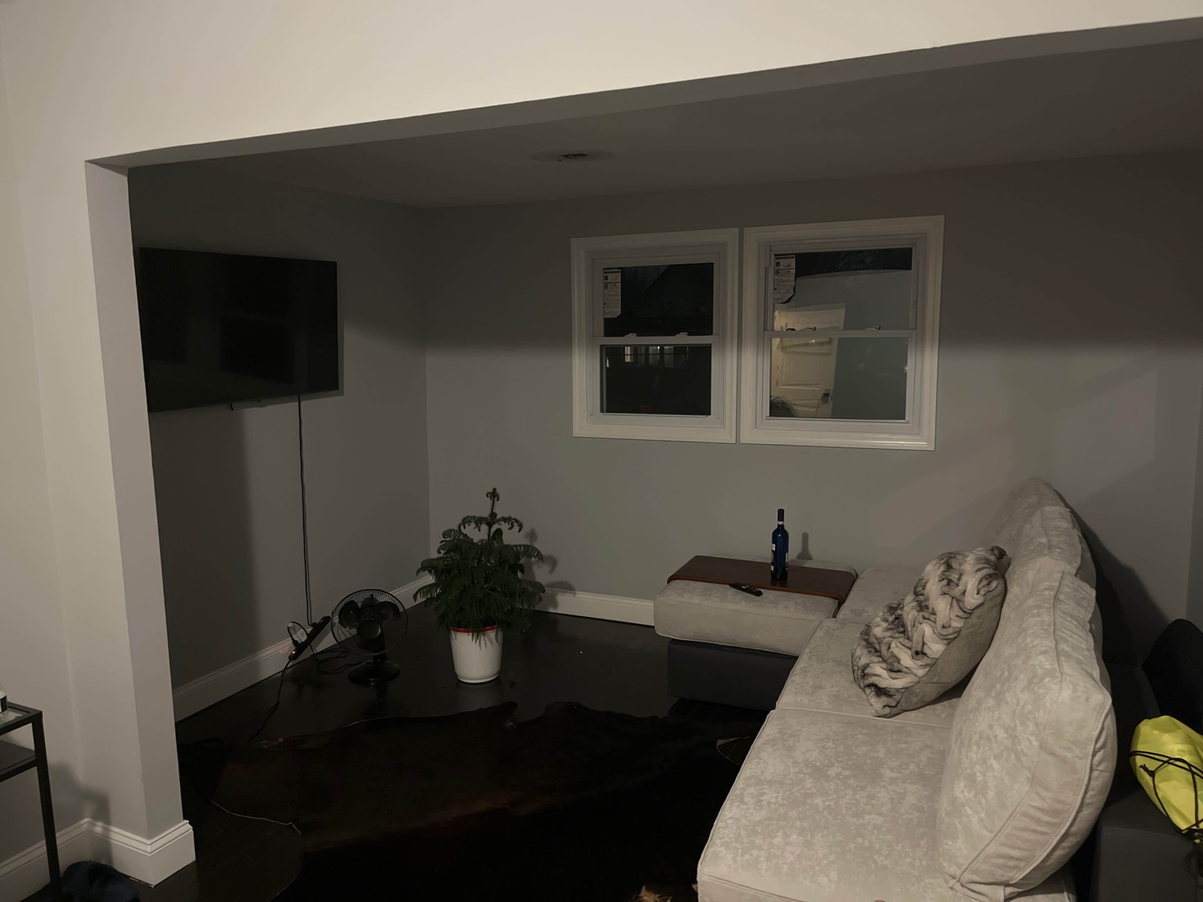 A living room space with a light-colored sofa, a television mounted on the wall, and a small plant on a wooden table.