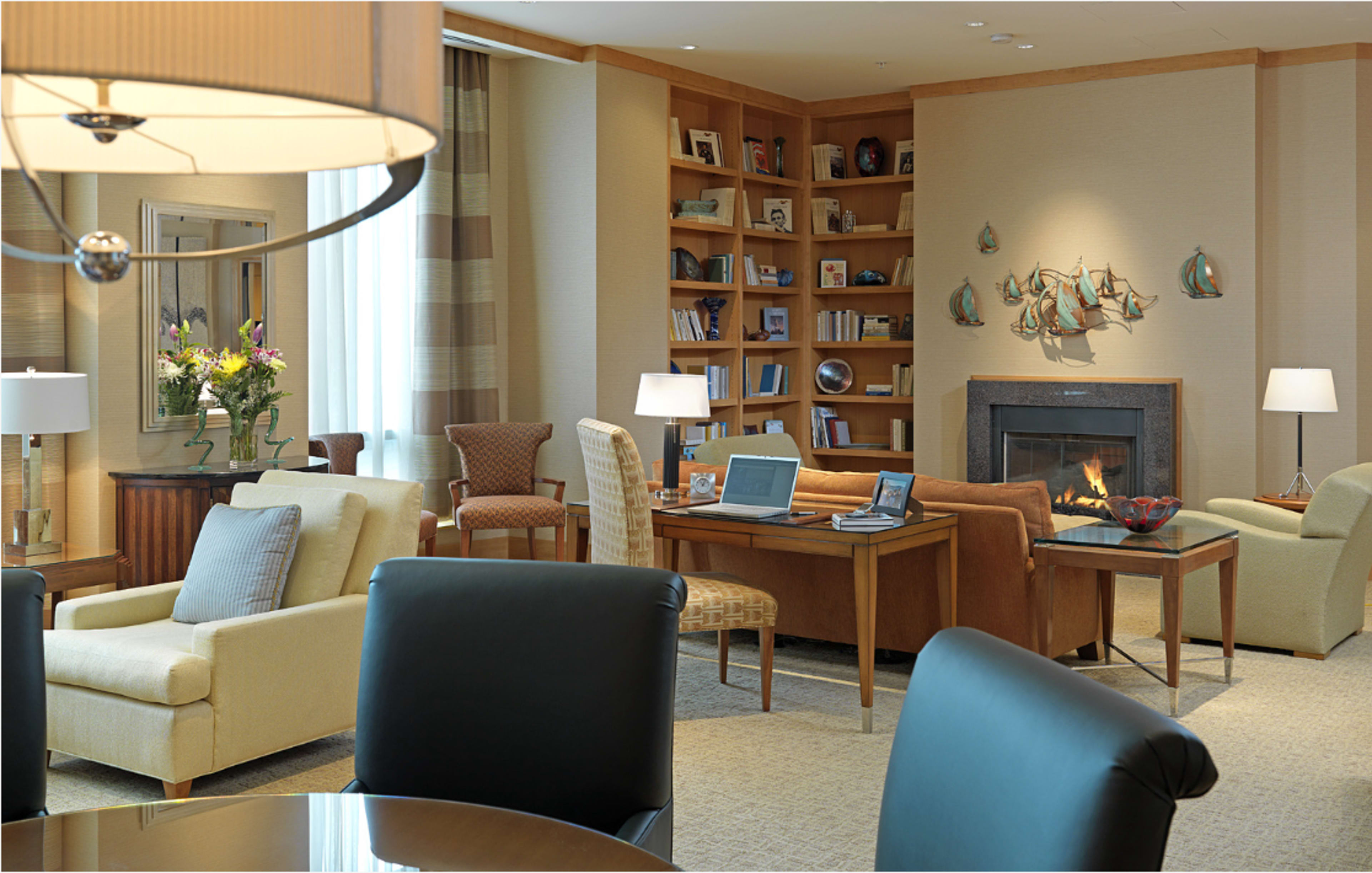 The image shows a modern sitting area in a hotel lobby featuring comfortable seating, a bookshelf, and a fireplace.