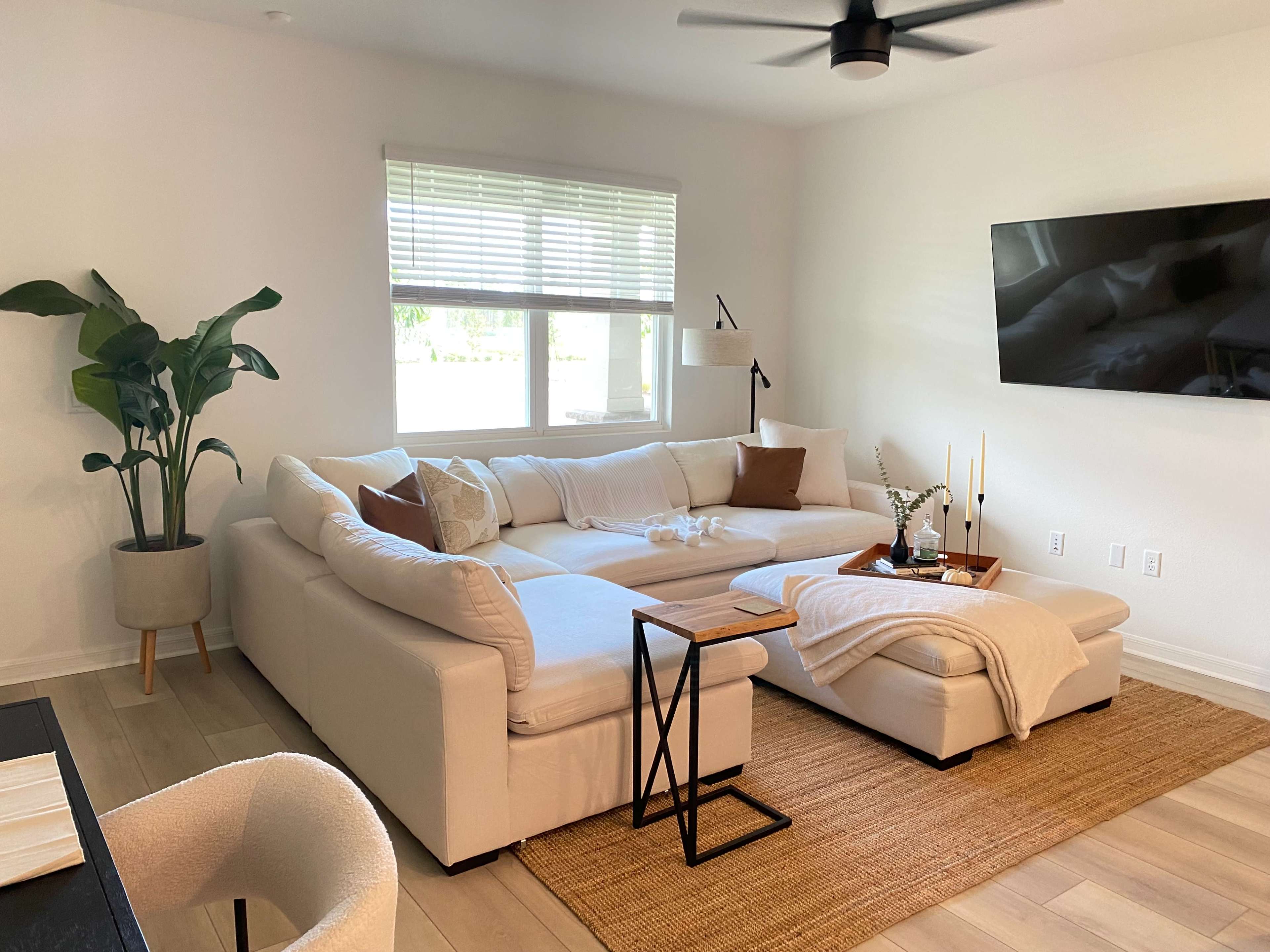 A modern living room features a large white sectional couch, a coffee table, and a potted plant next to the window.