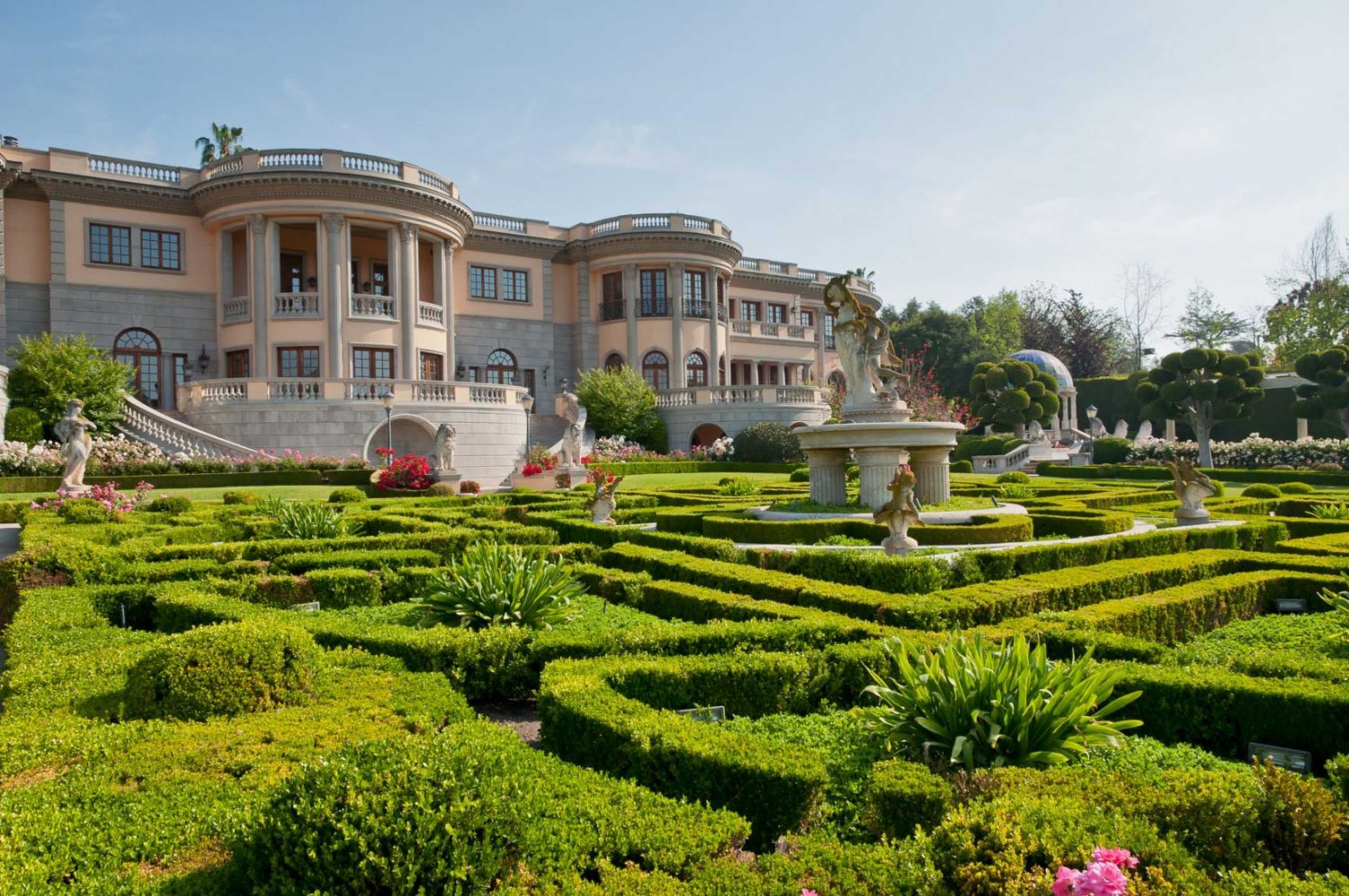 A large mansion surrounded by meticulously landscaped gardens and symmetrical hedges.