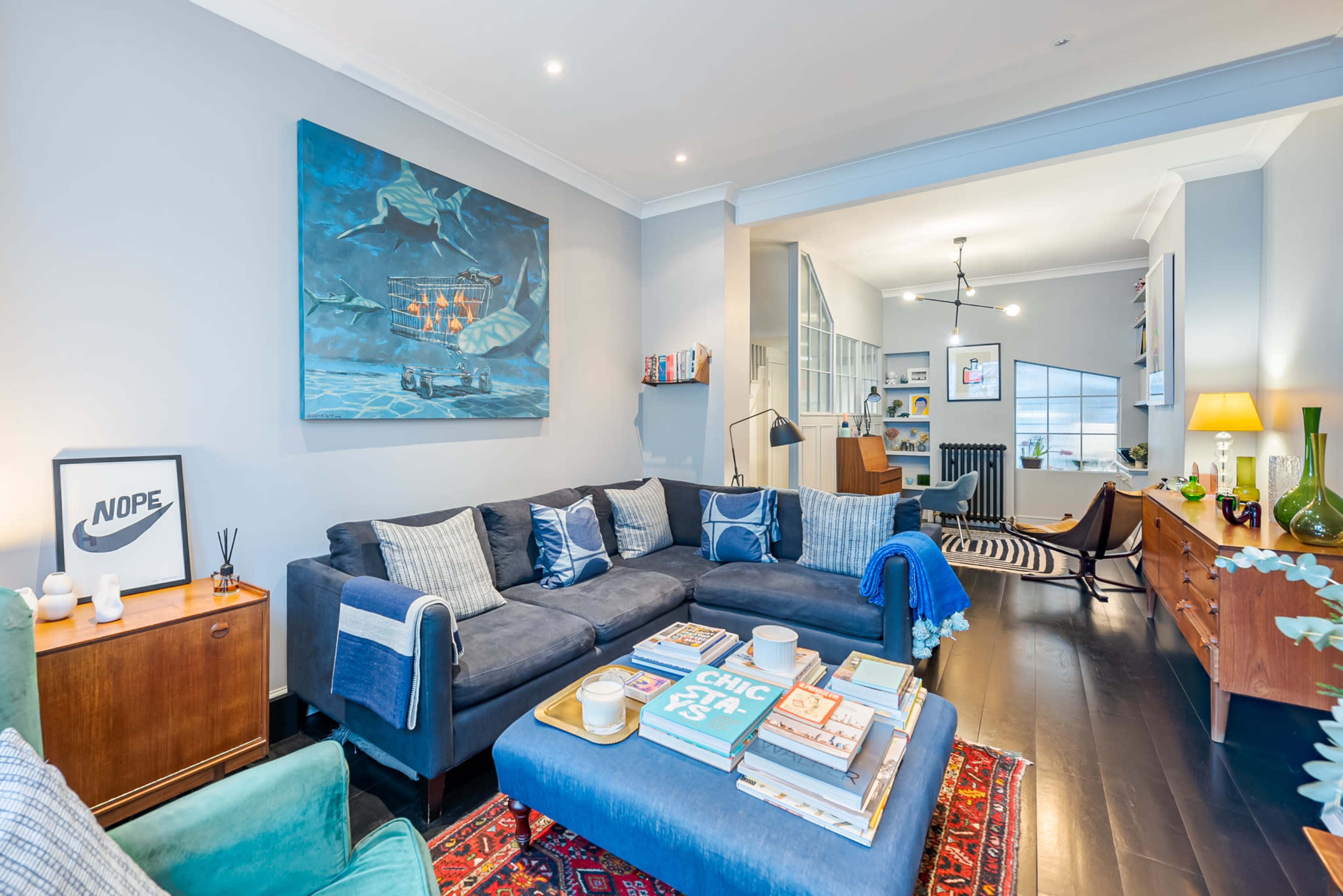 A modern living room features a dark blue sectional sofa with patterned cushions, a large artwork on the wall, and a coffee table stacked with books and decor.