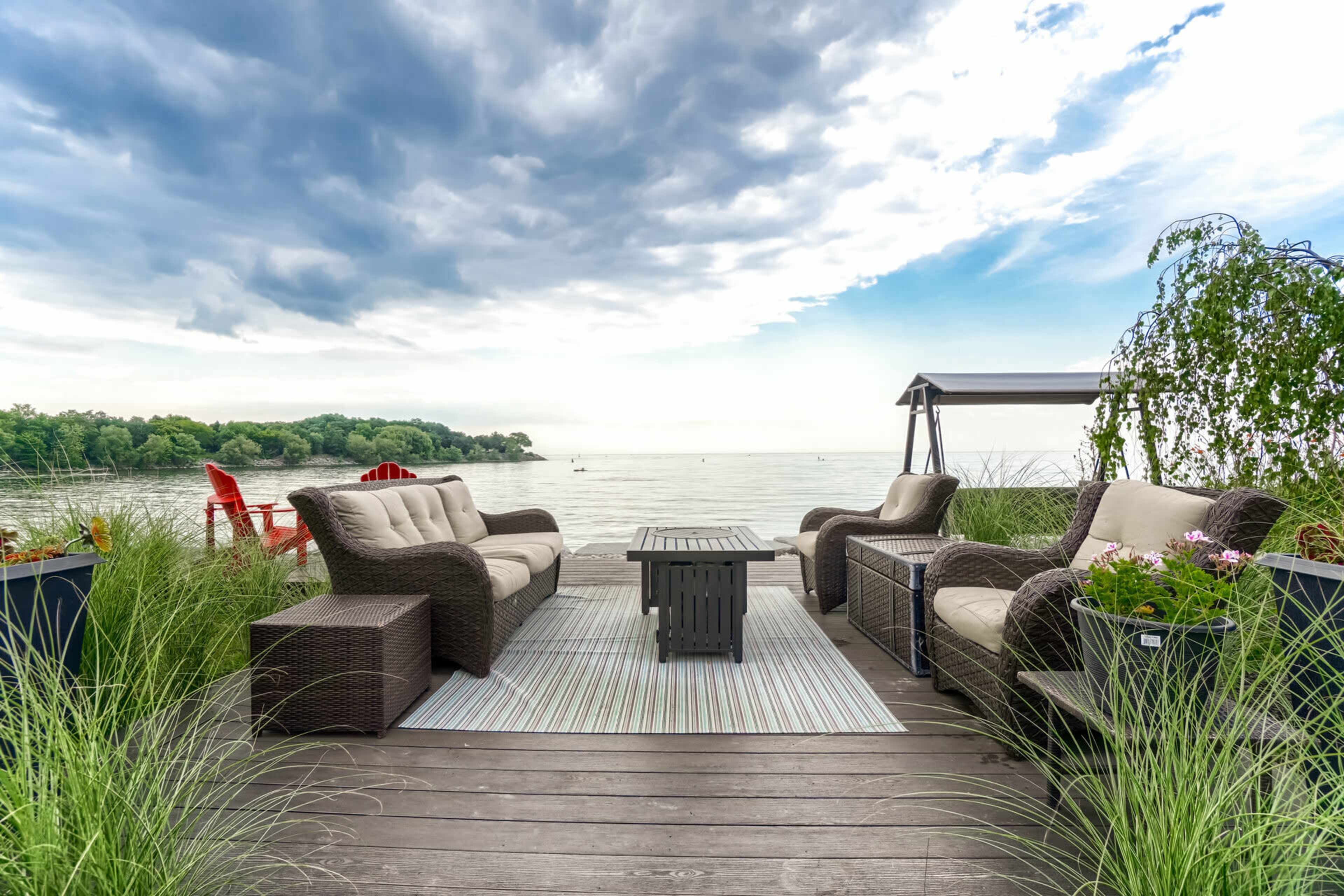 A seating area with two sofas and a coffee table overlooks a calm lake with trees in the background.
