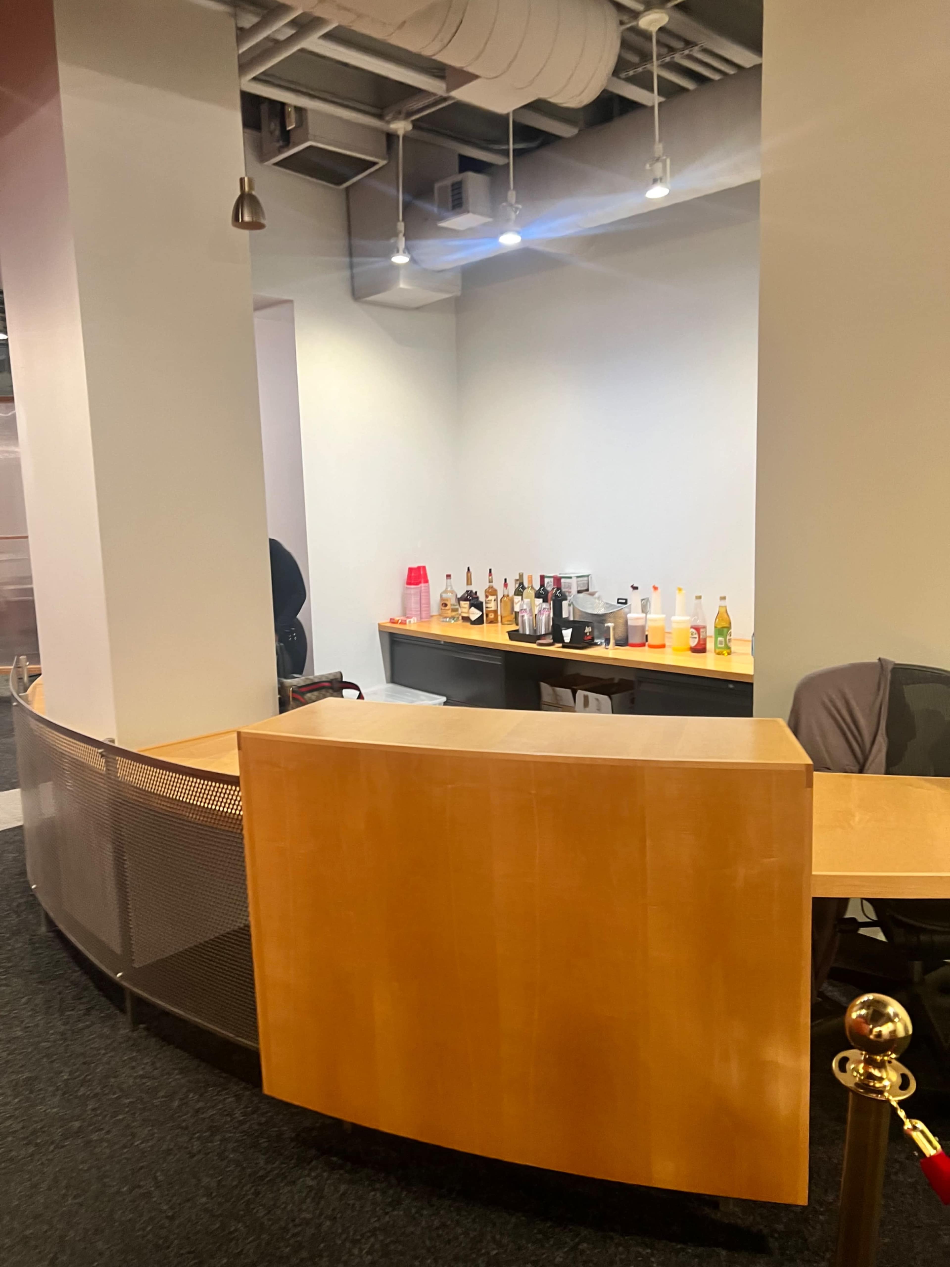 The image shows a wooden reception desk with a variety of bottles displayed on a countertop in an office setting.