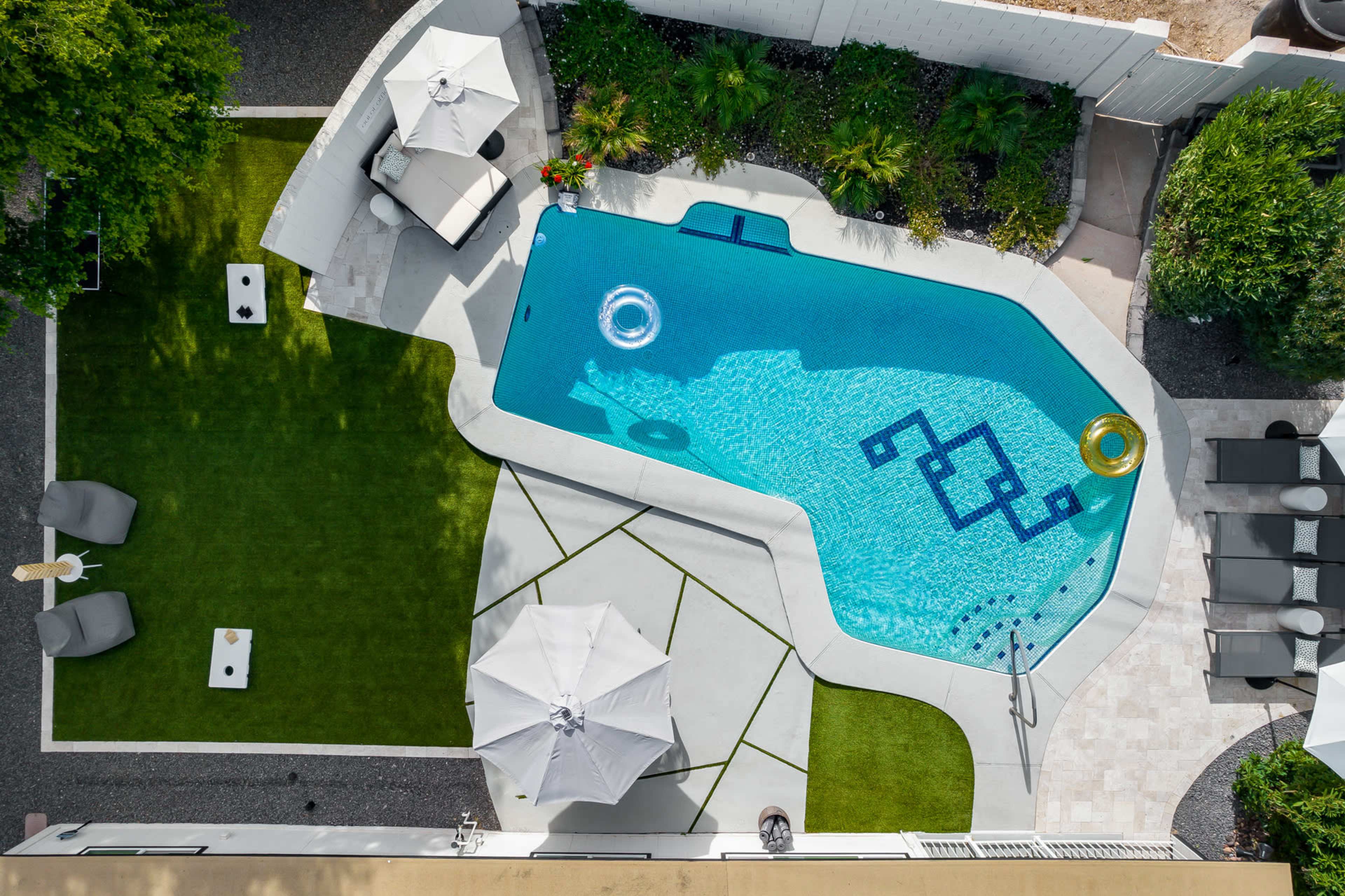An aerial view of a landscaped backyard featuring a swimming pool, lounge chairs, and various plants.
